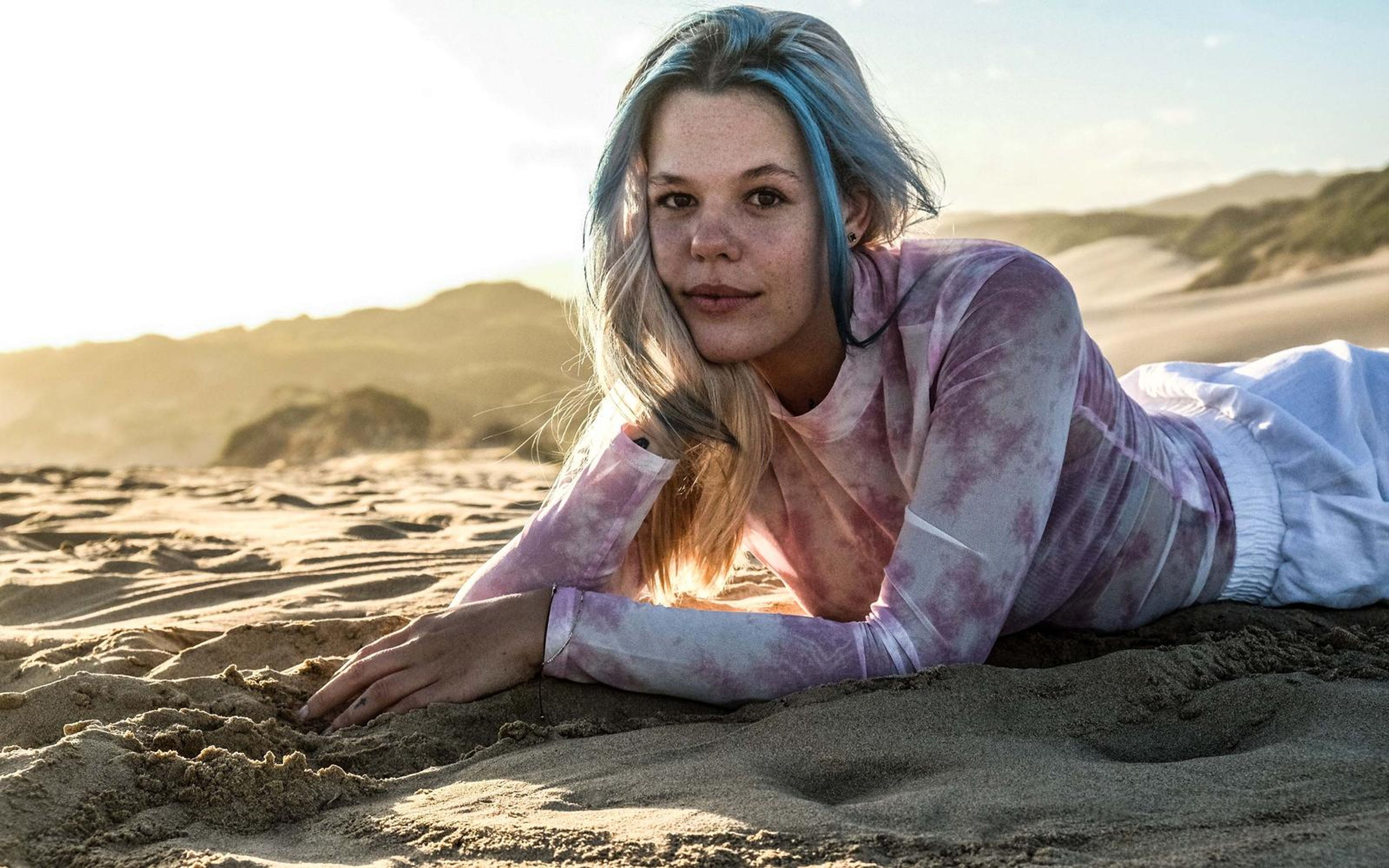 Woman propped on her forearms on the sand looking directly at the camera