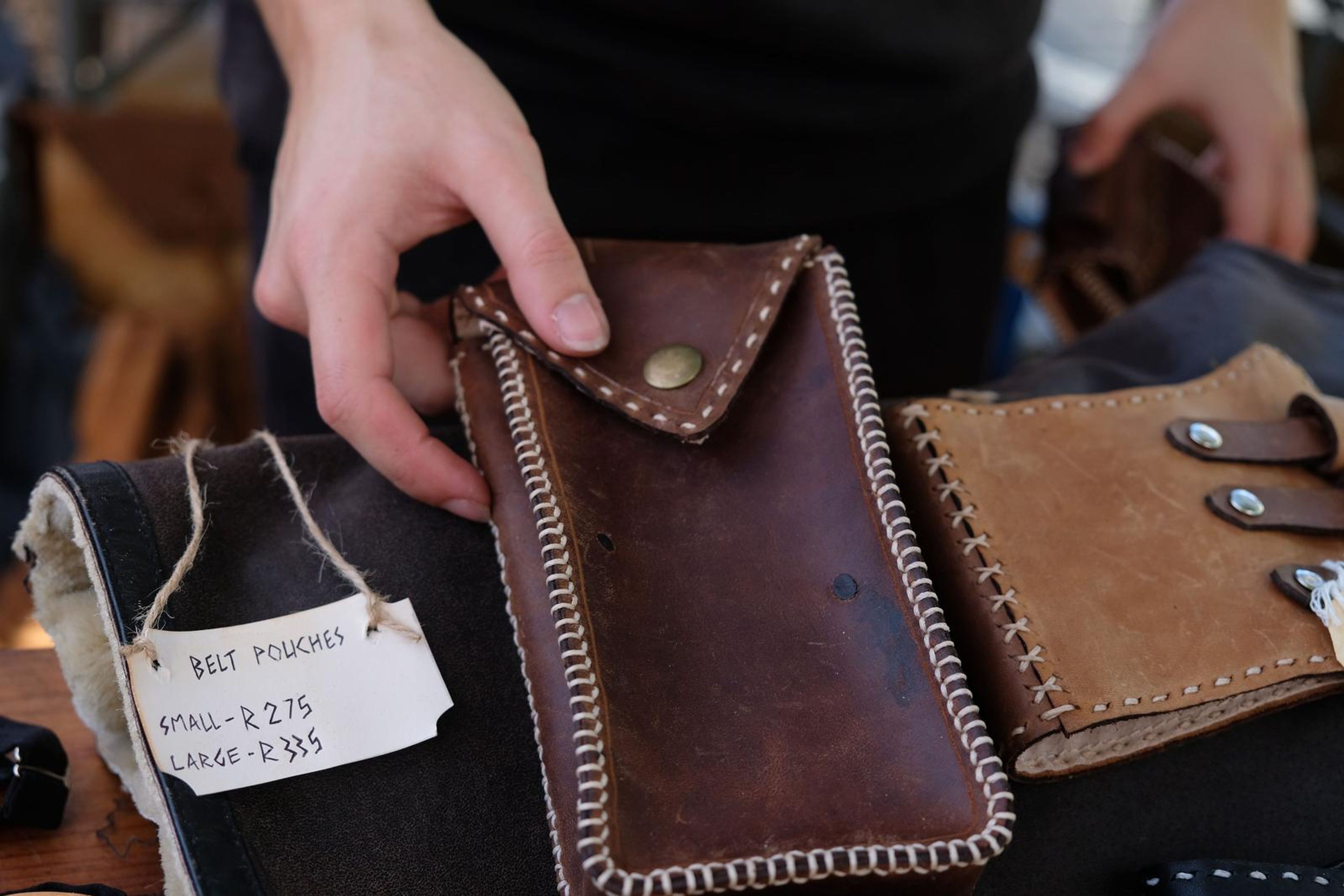 Hand holding a brown leather belt pouch beside tan buckled wrist pieces