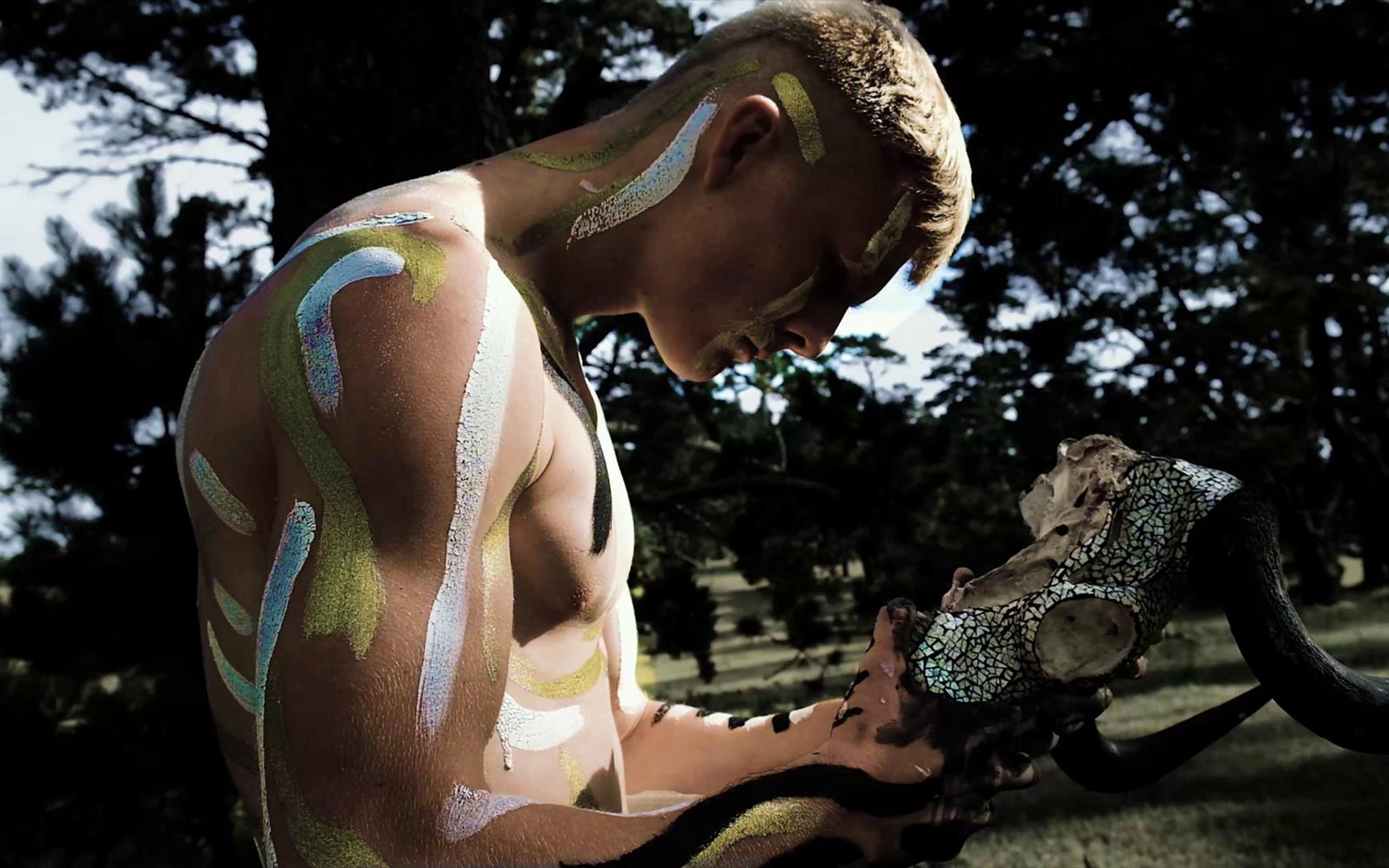Performer in side profile painting his arm with a skull in his other hand