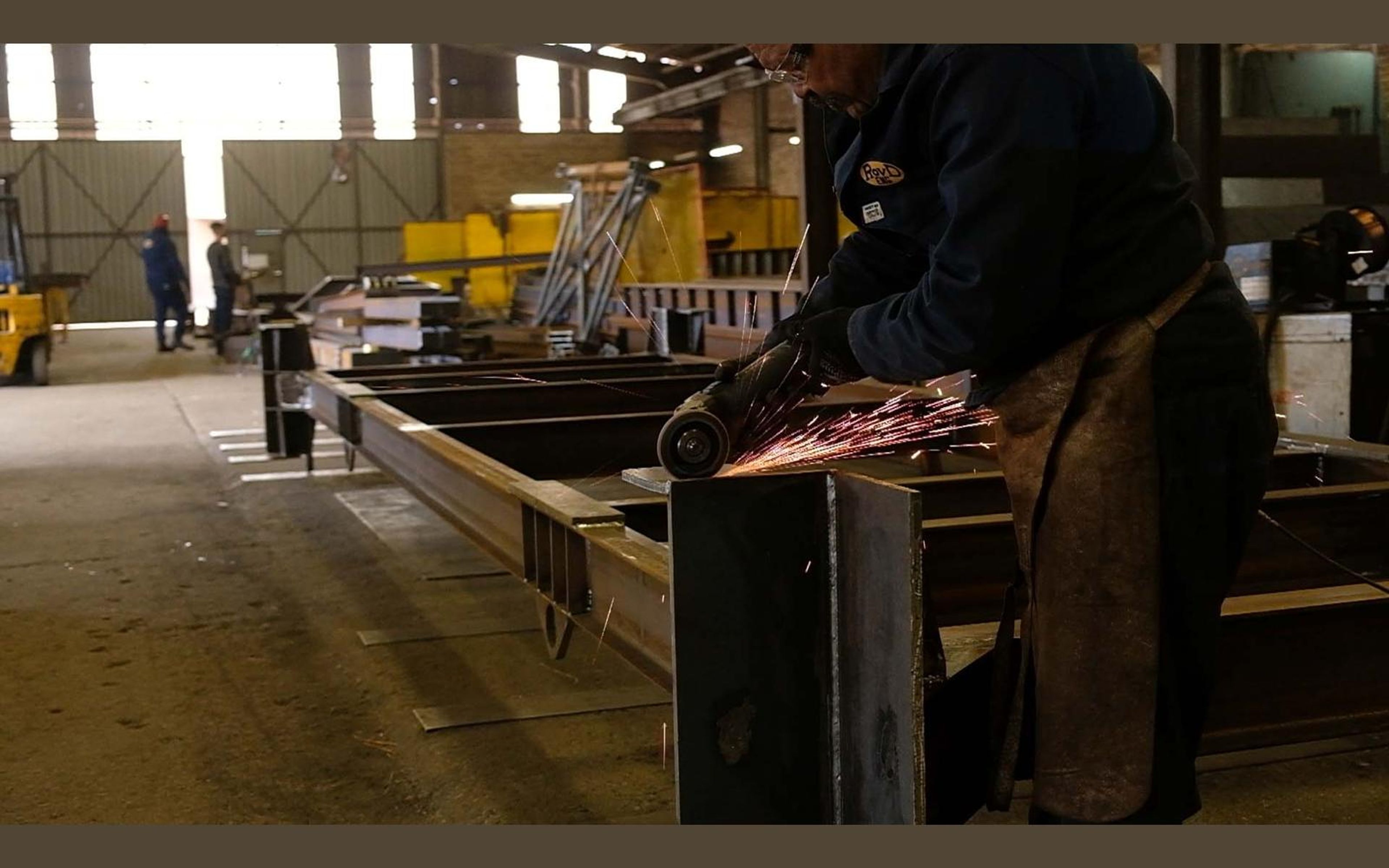Fabricators at work among steel beams in the shop