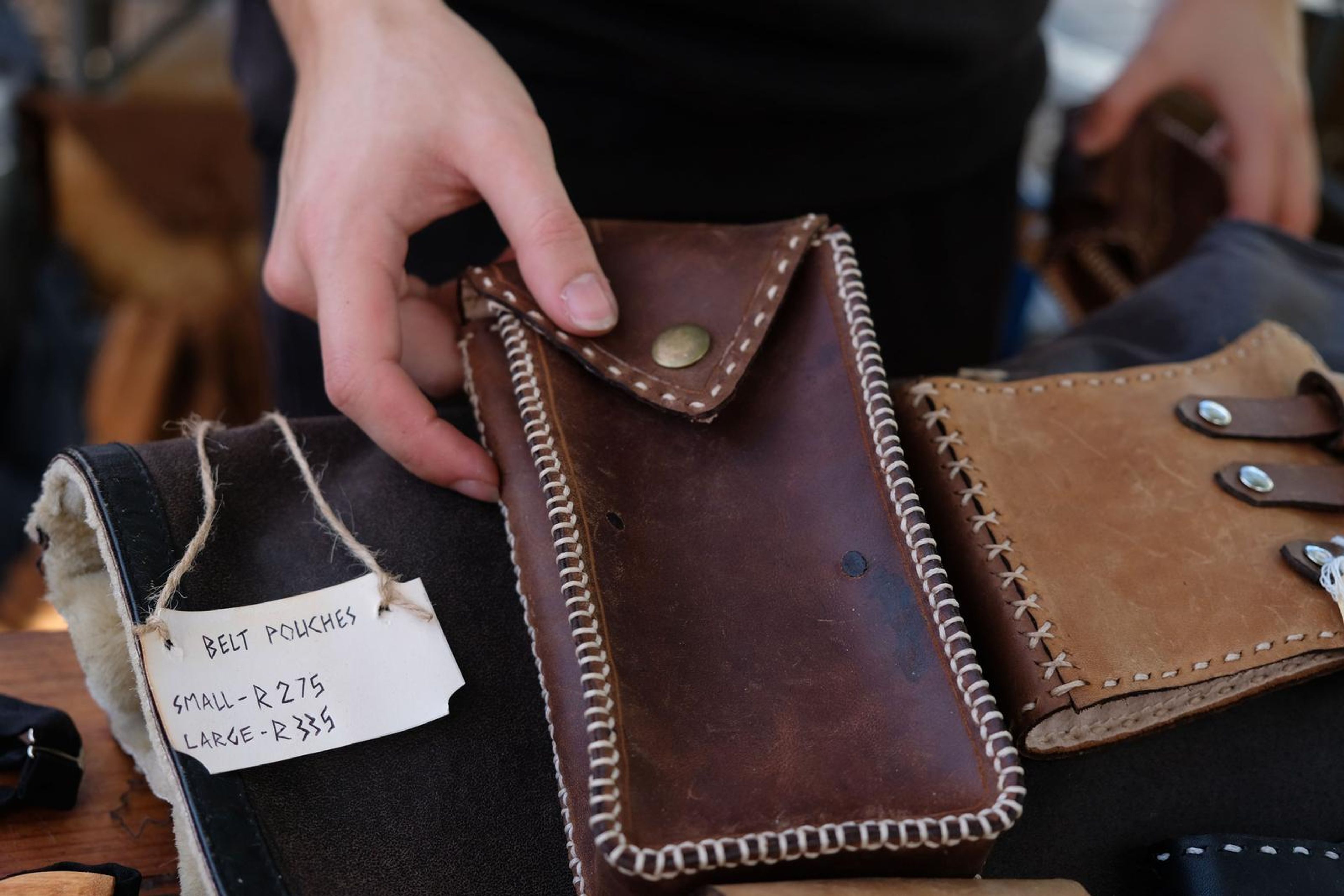 Hand holding a brown leather belt pouch with a price tag