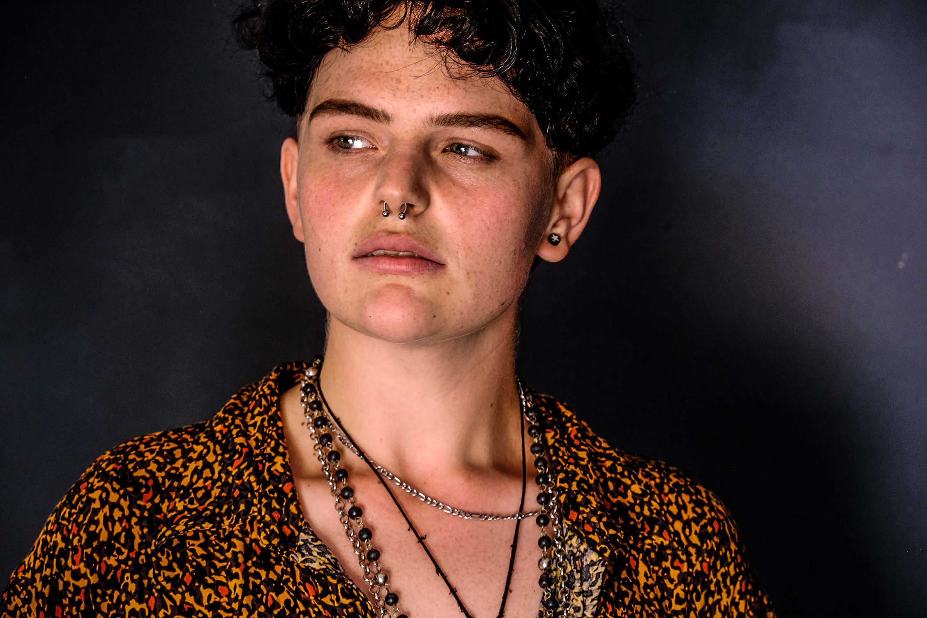 Portrait, subject in a patterned shirt with layered necklaces, looking to the side