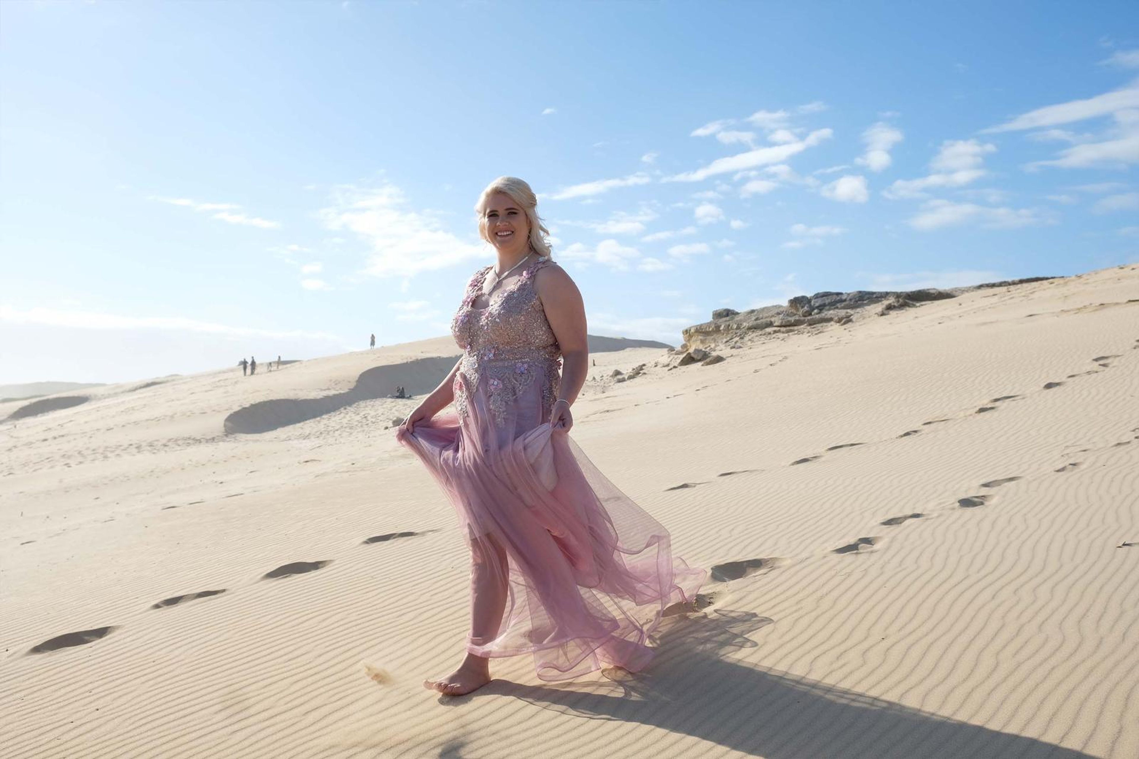 Holding the gown on a sunlit sand dune