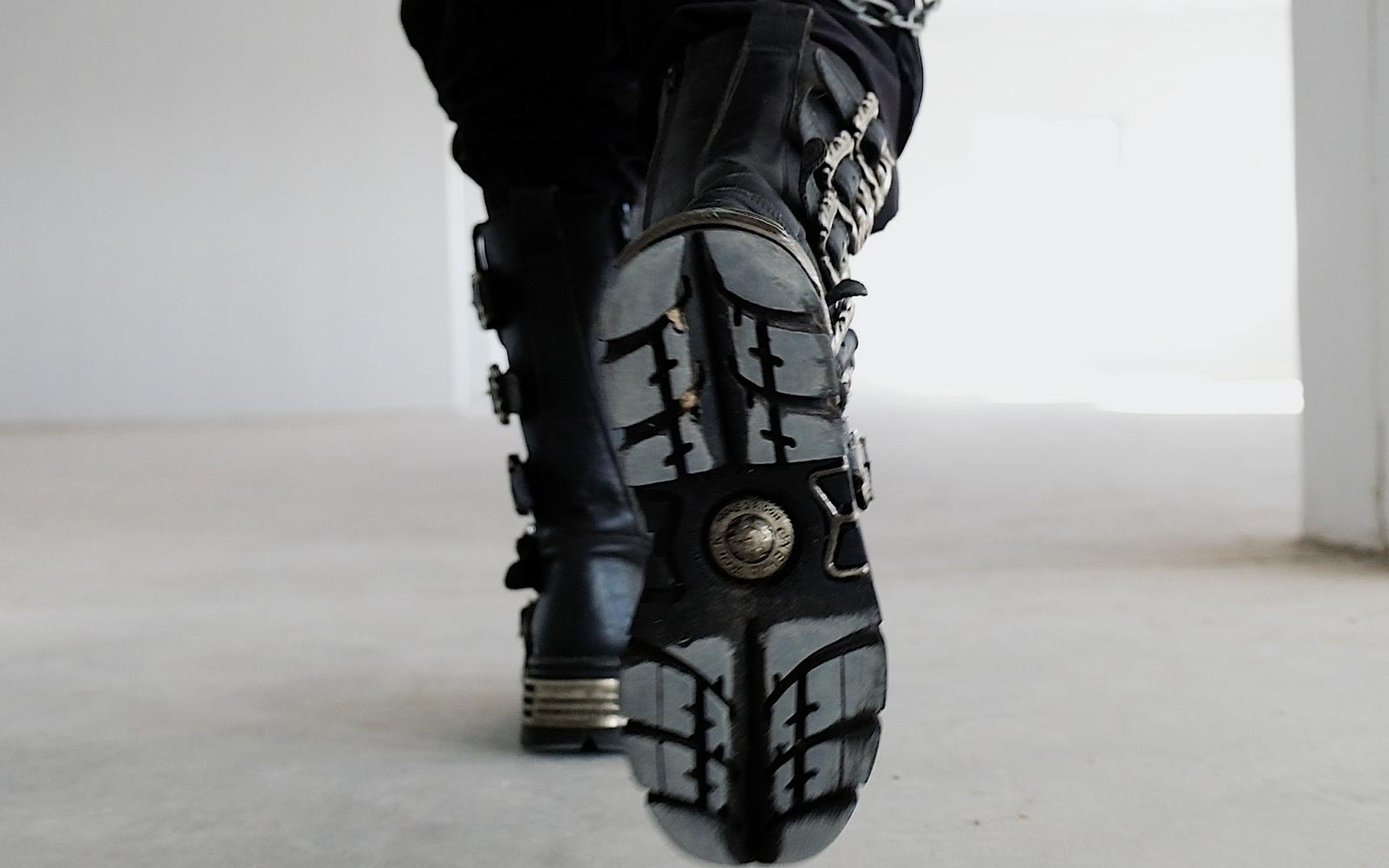 Underside of a black boot sole with a round emblem as the foot lifts away on a pale floor