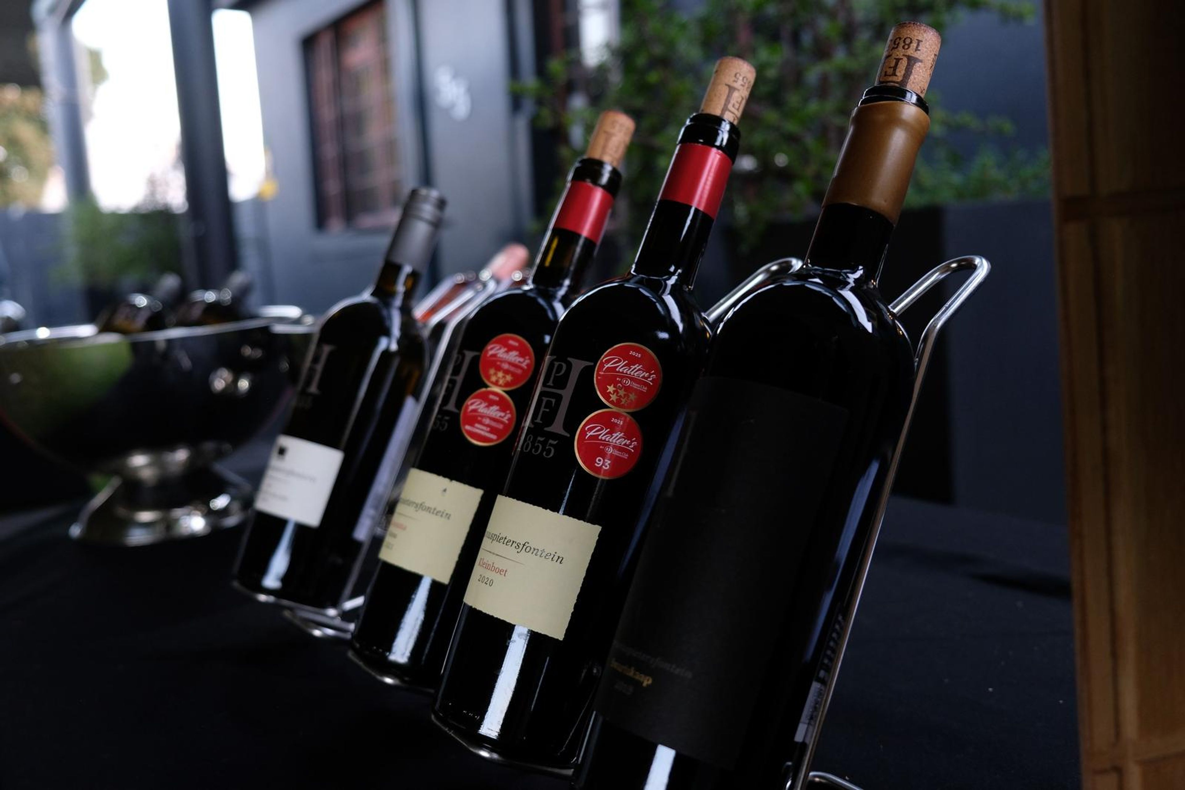 Red and white wine bottles on a metal rack at the tasting table