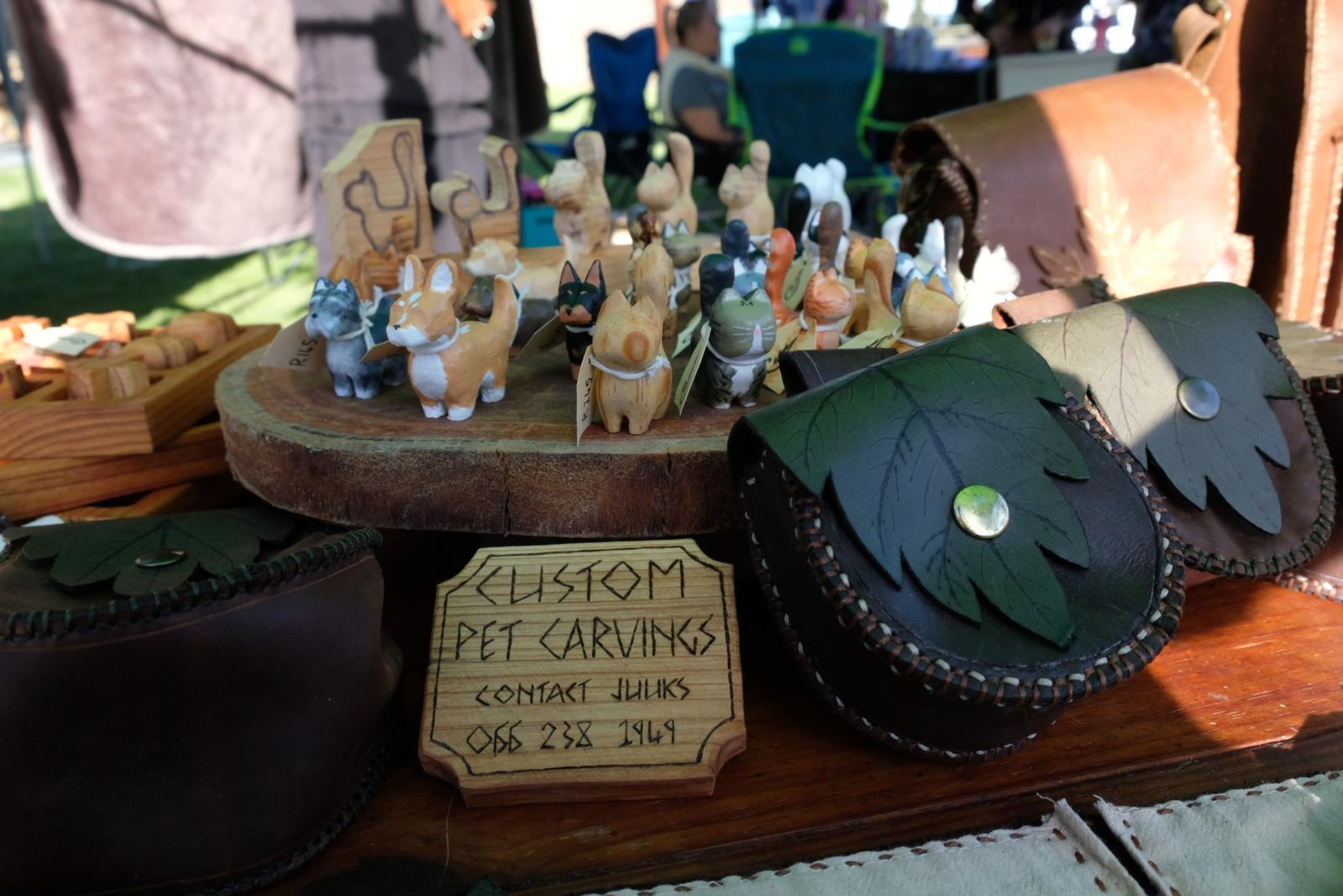 Custom Pet Carvings display with carved figures and black leaf-shaped leather pouches