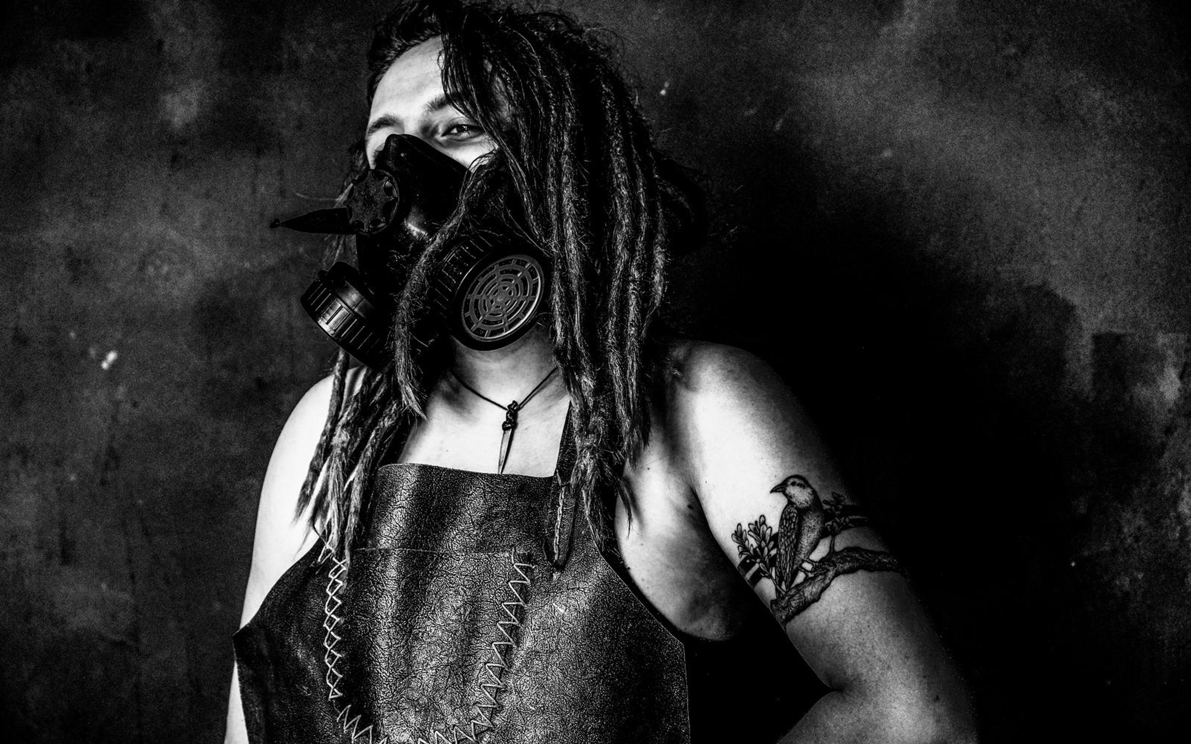 Black and white version of a dreadlocked woman in a spiked respirator mask and leather apron with an arm tattoo