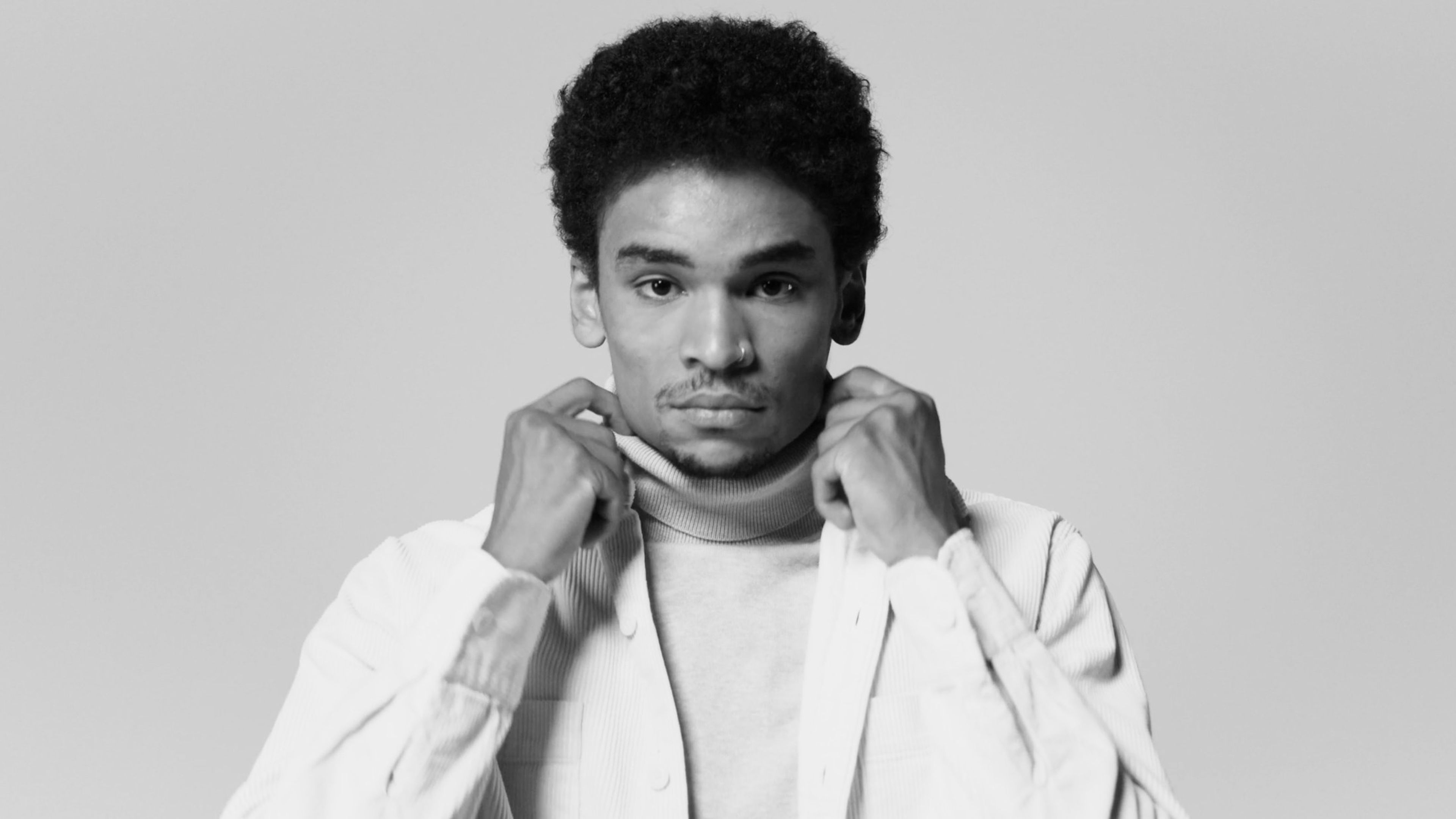 Man in a white jacket pulling up his collar against a grey studio backdrop