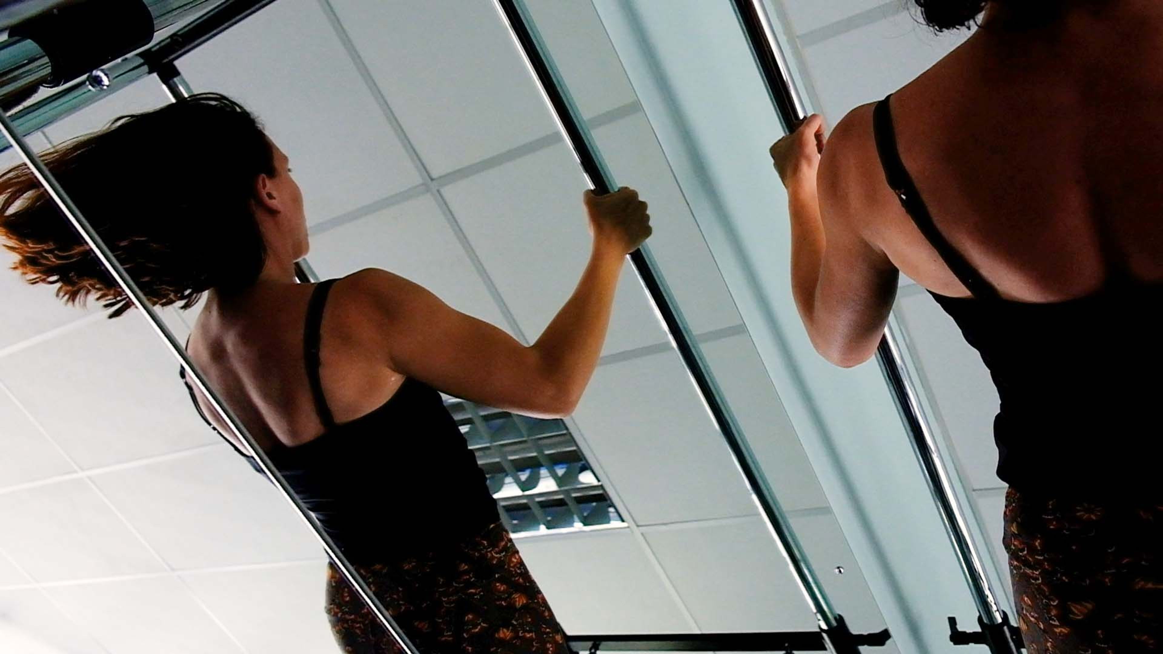Two women exercising at a Pilates frame, one reflected in the mirror