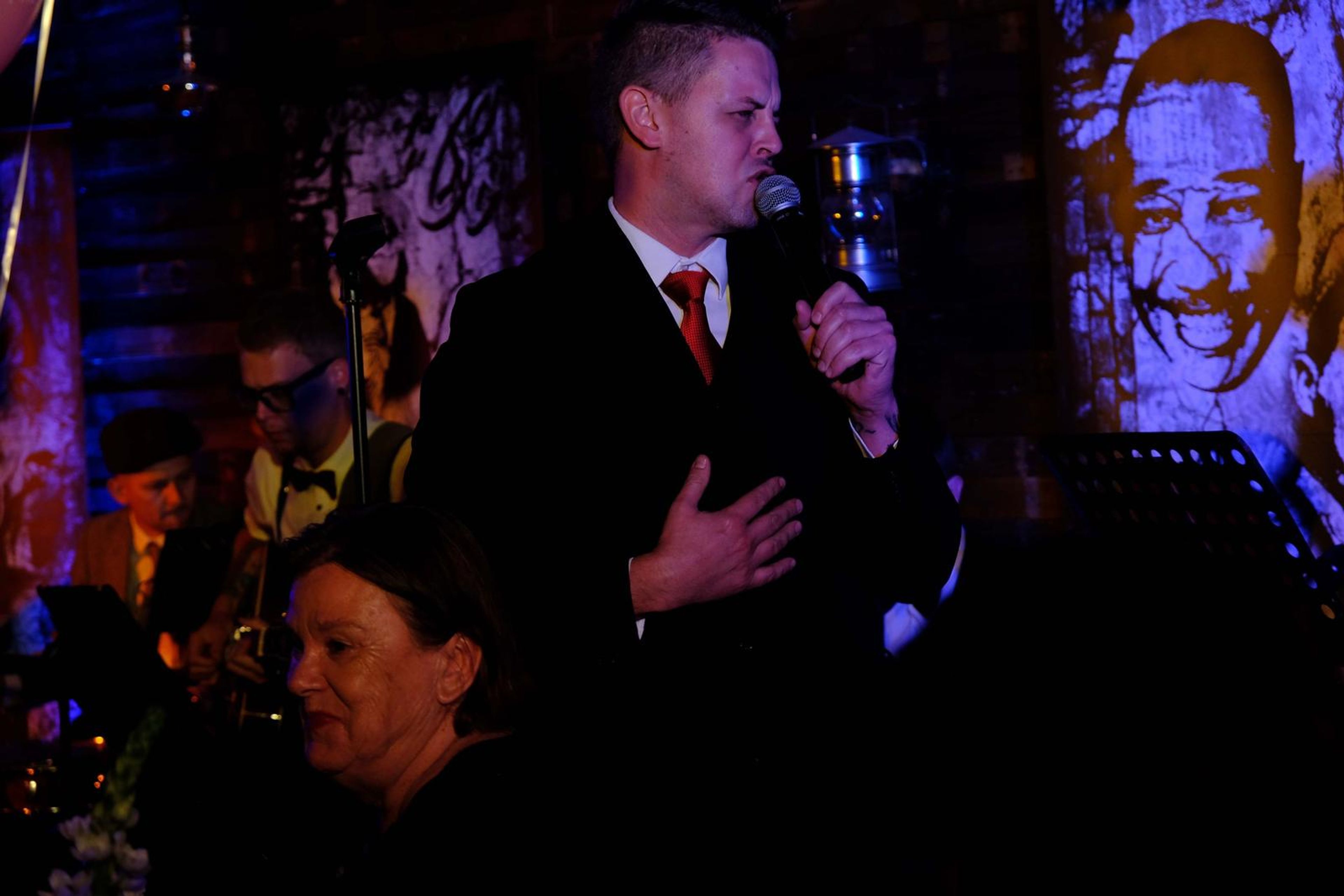 Singer in a suit and red tie with his hand over his heart