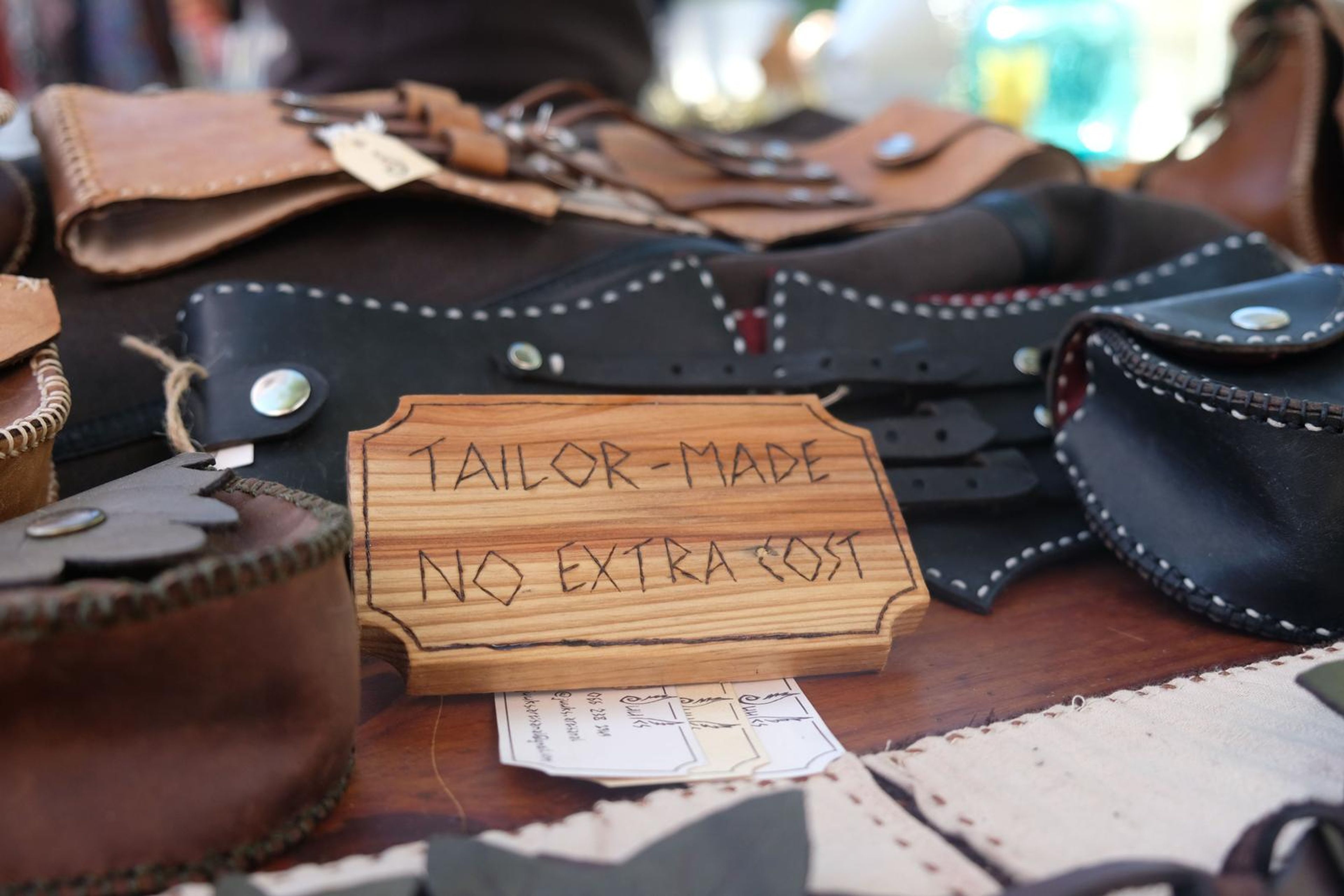 Black leather pouch and corset belts beside a Tailor-Made No Extra Cost sign