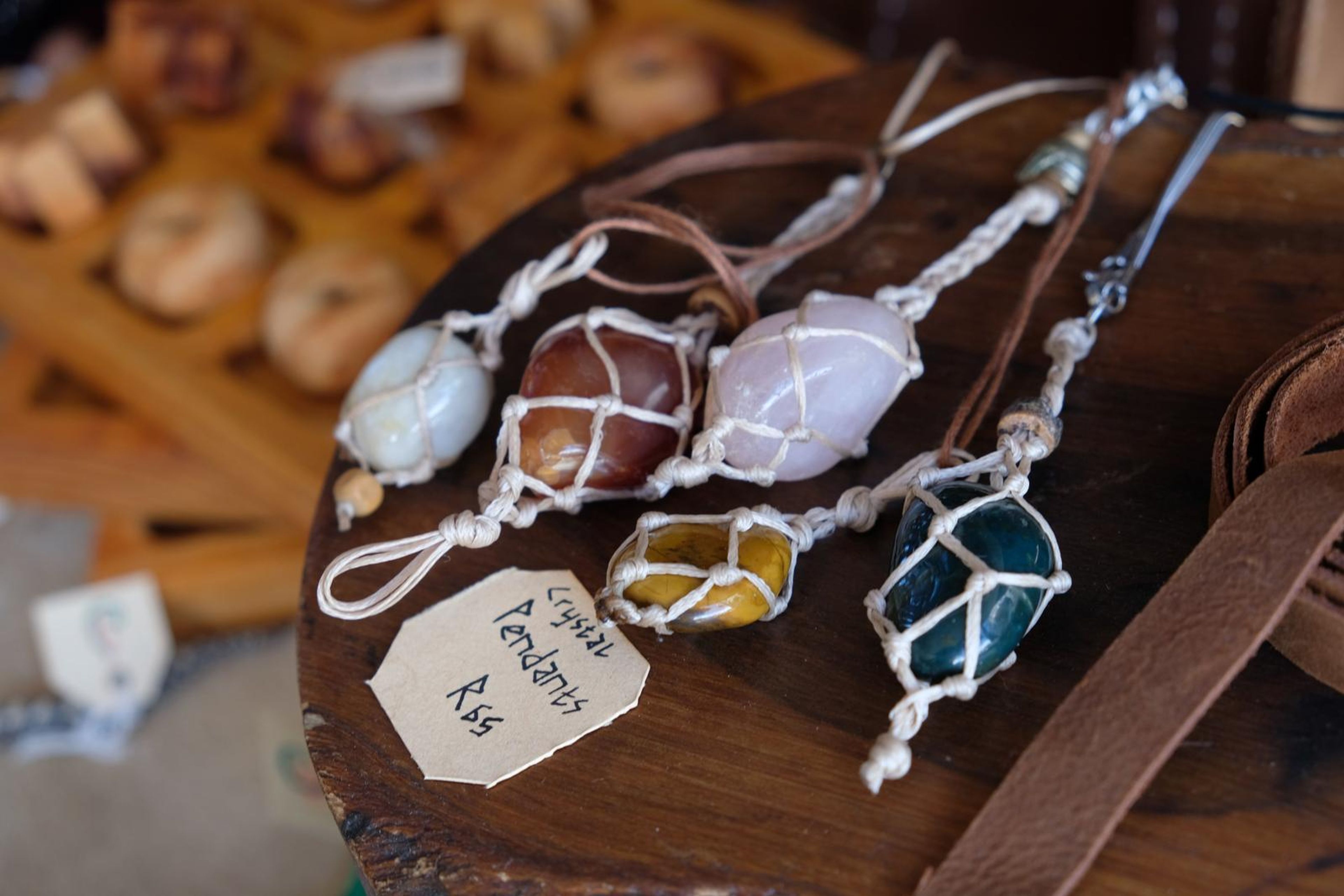 Wire-wrapped crystal pendants on a wooden stool with a handwritten price tag
