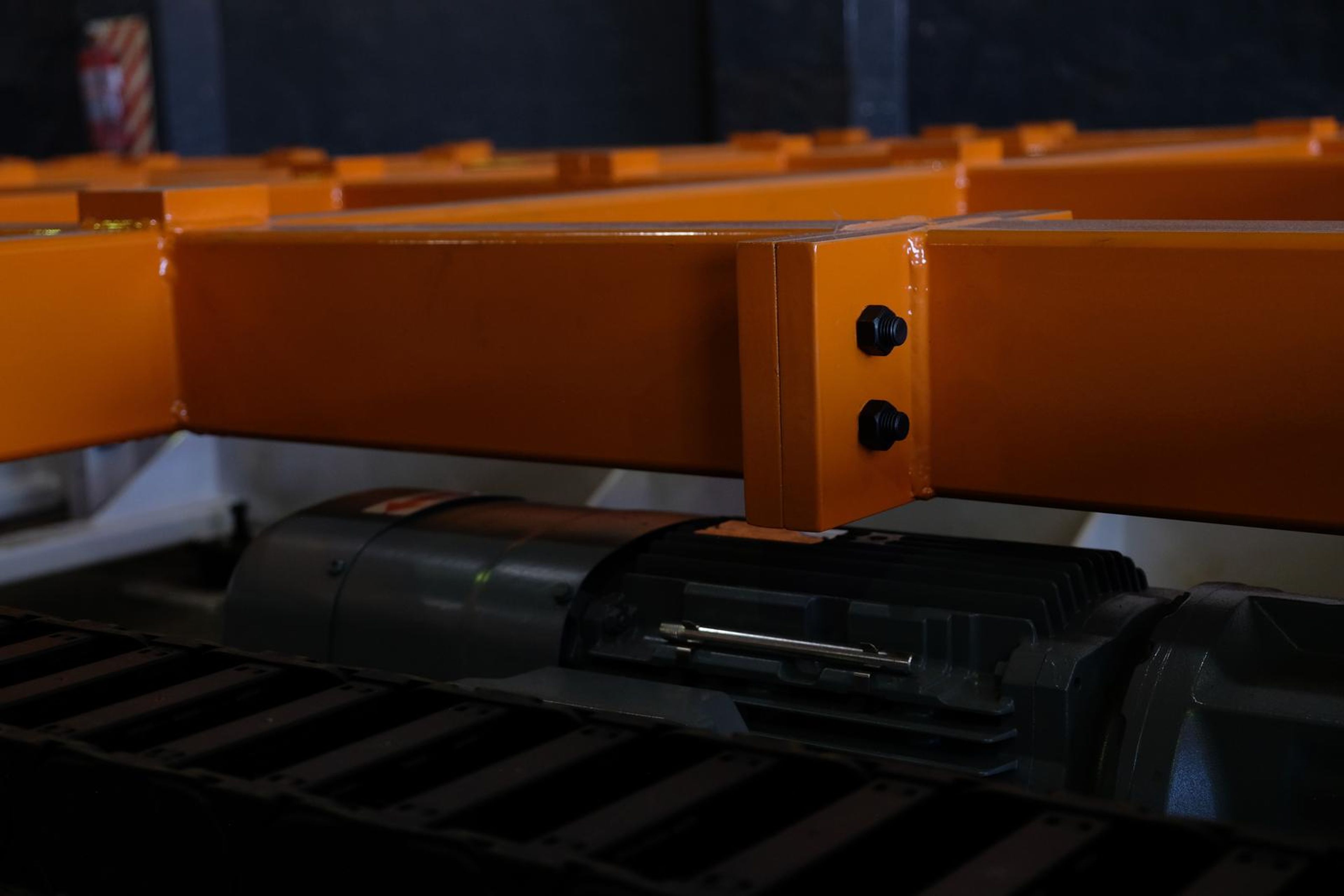 Orange box beam joint with two black bolts above a drive chain