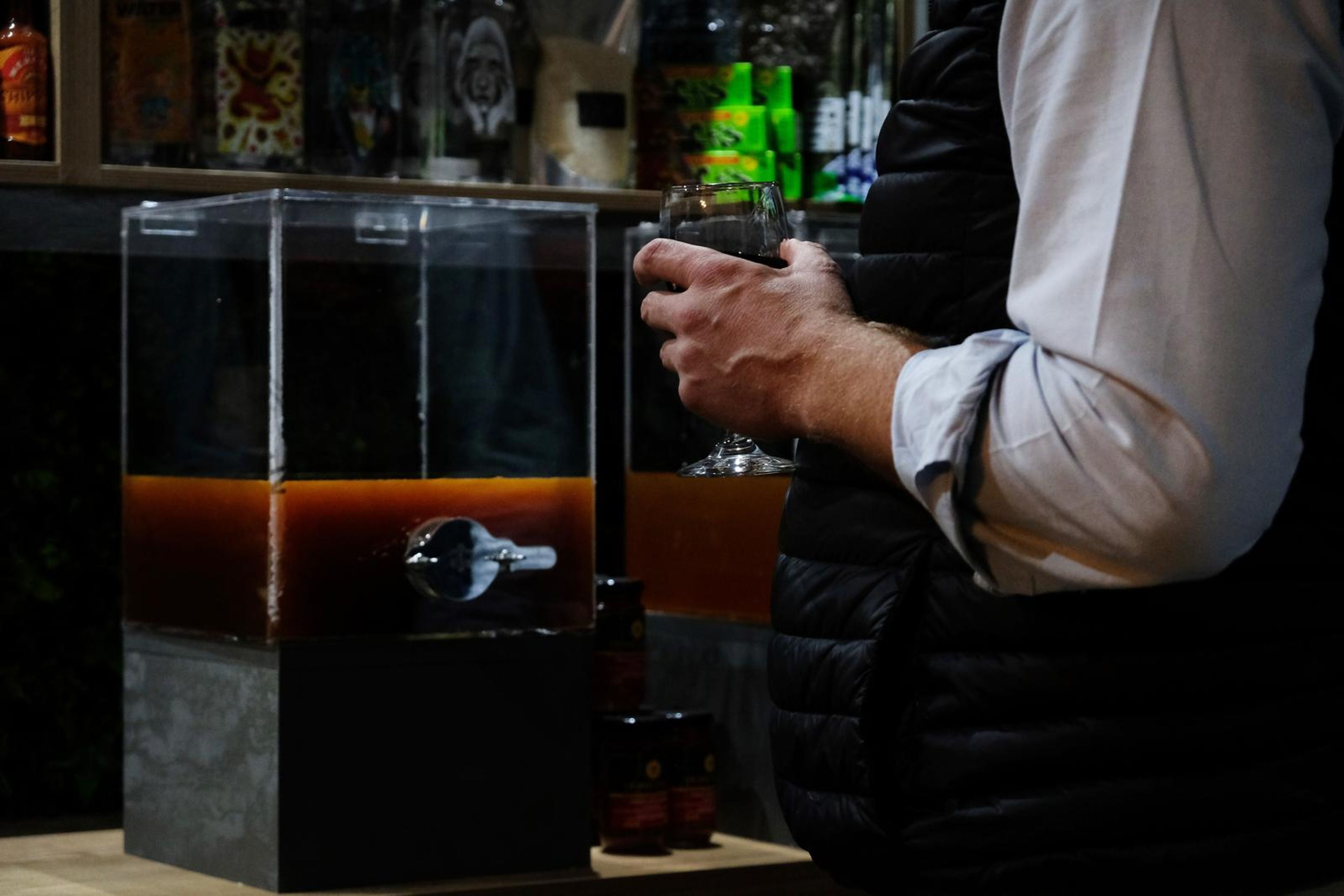 Drinks dispenser filled with dark liquid beside guests at the counter