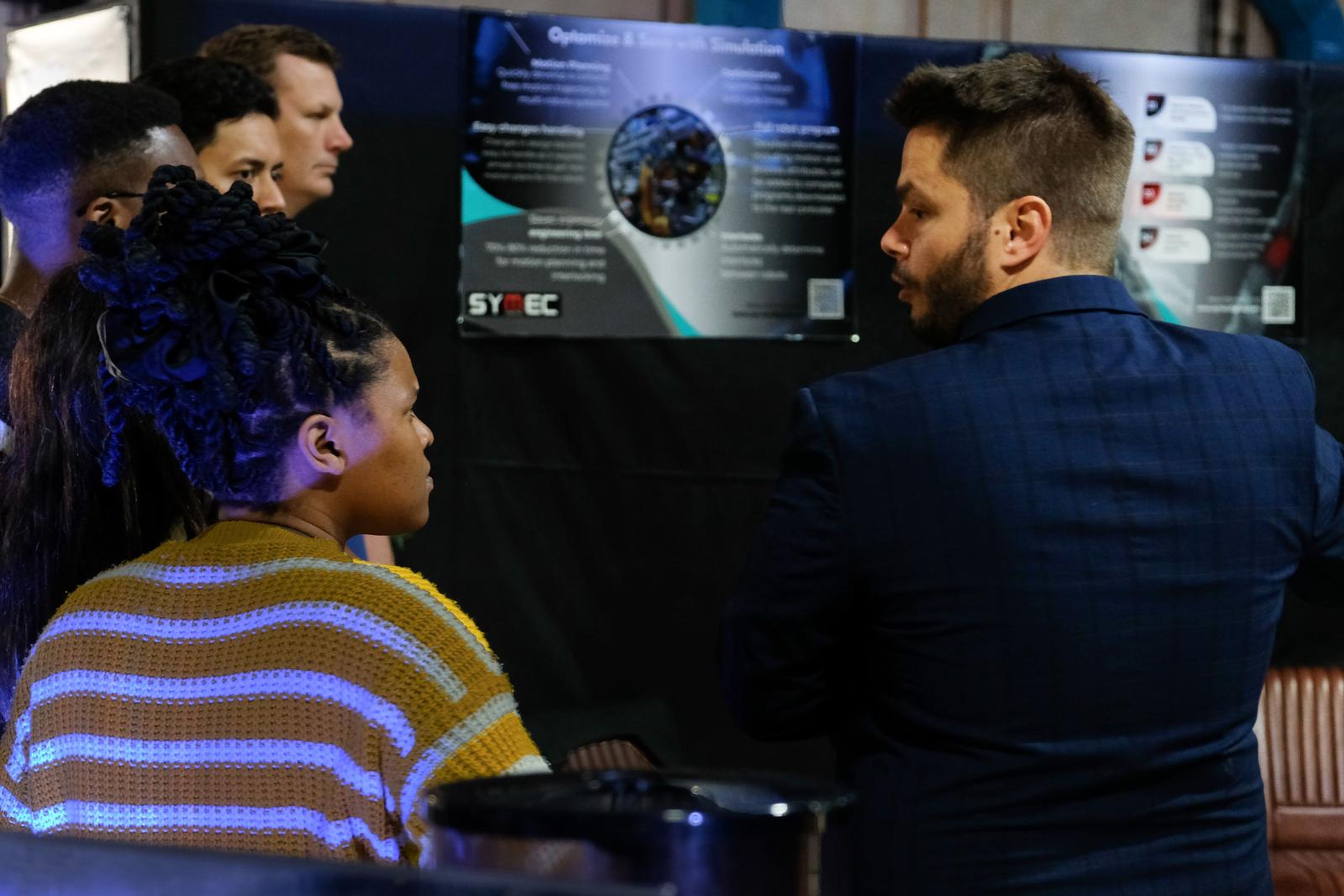 Visitors listening to a Symec team member at a display panel