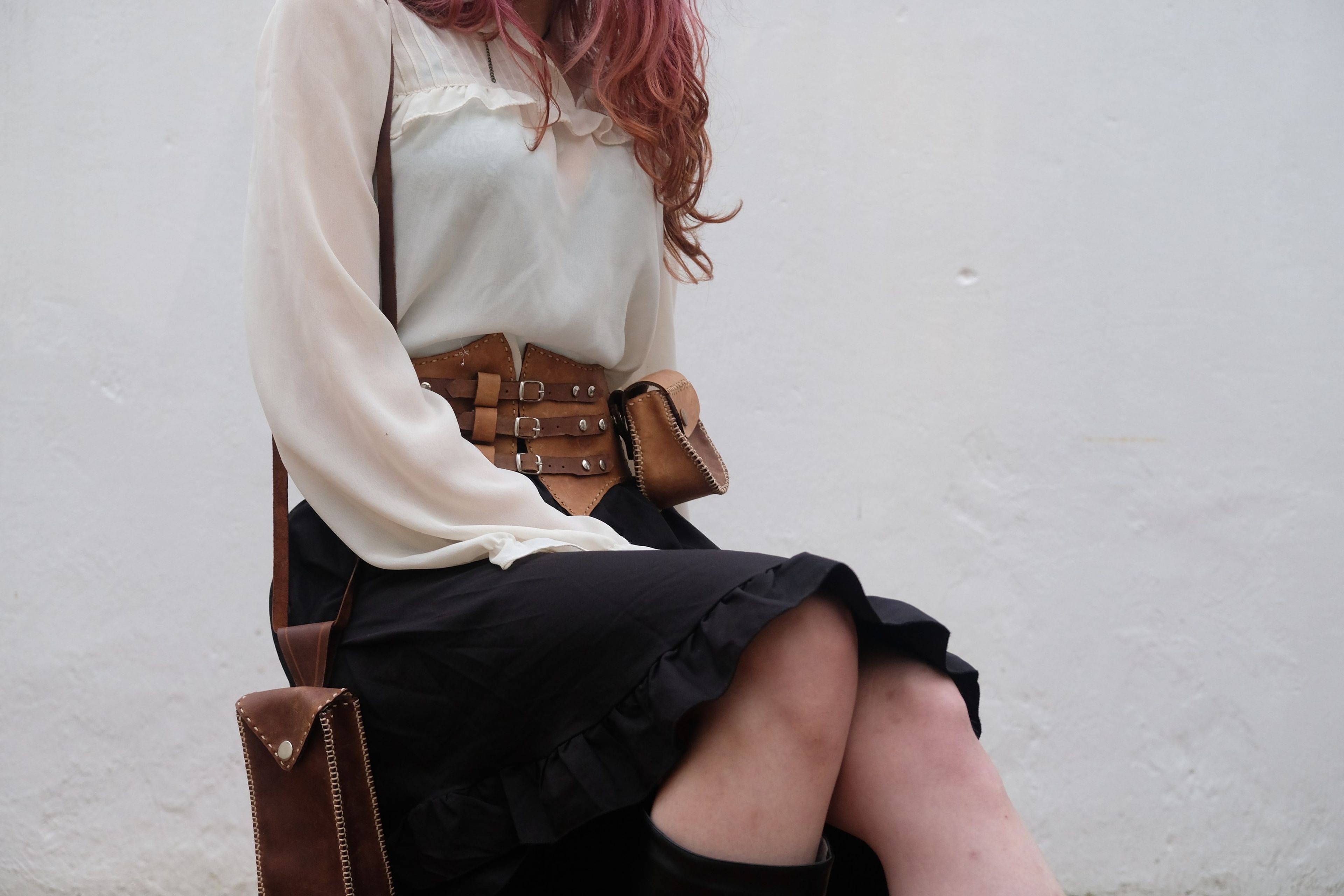 Woman wearing a tan leather corset belt with a round pouch and a brown phone bag