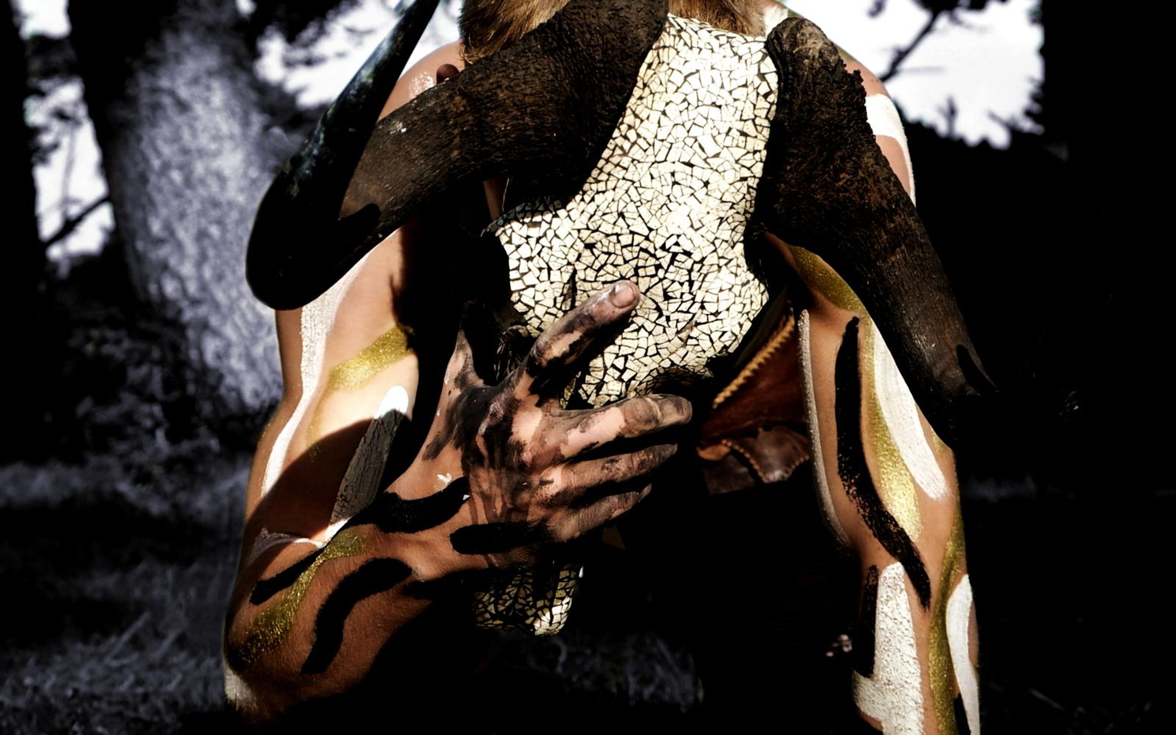 Performer crawling on all fours with a horned skull over his head, painted in gold and black stripes in a dark forest