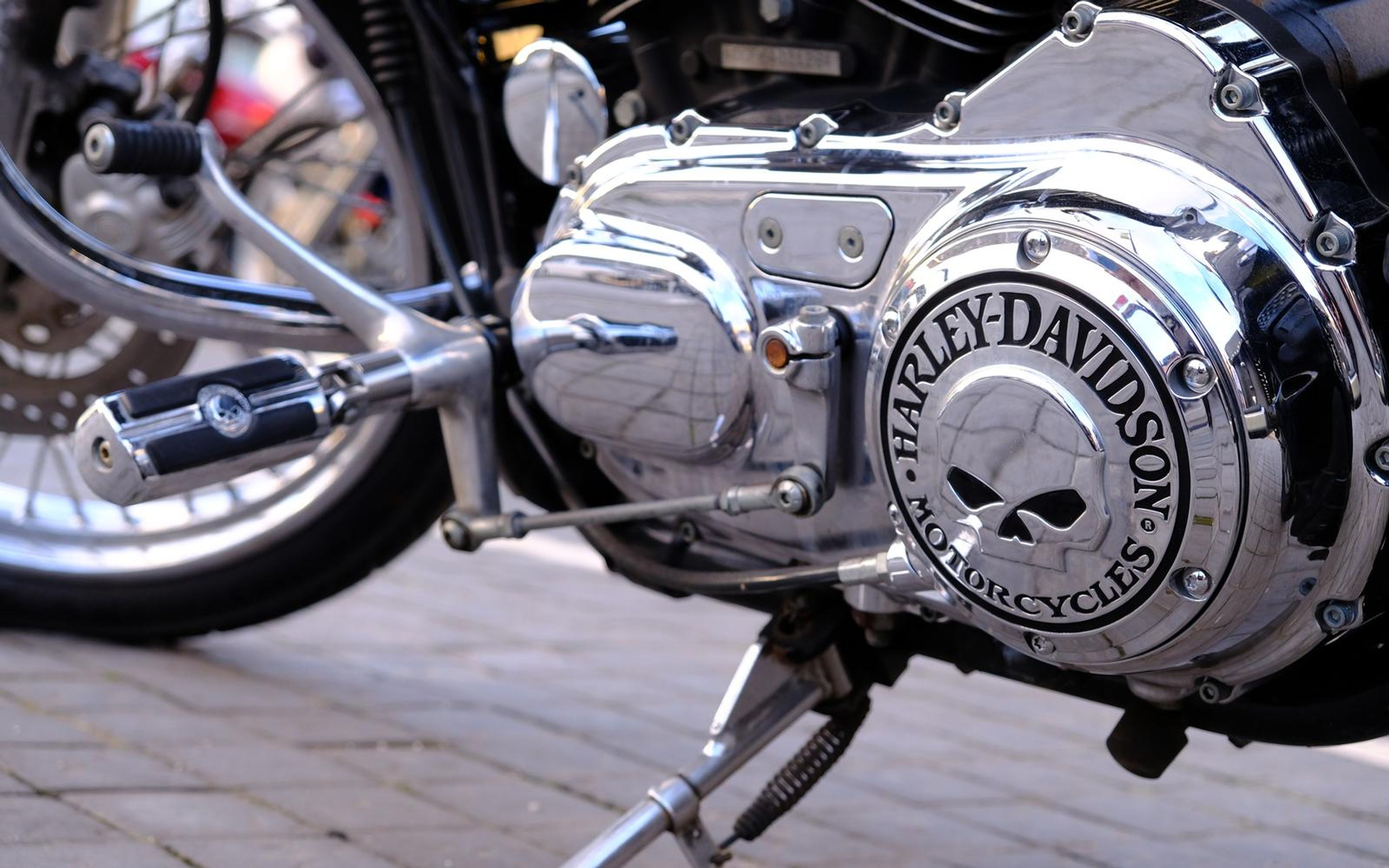 Polished chrome engine casing with an embossed skull logo and footpeg on a cobbled street