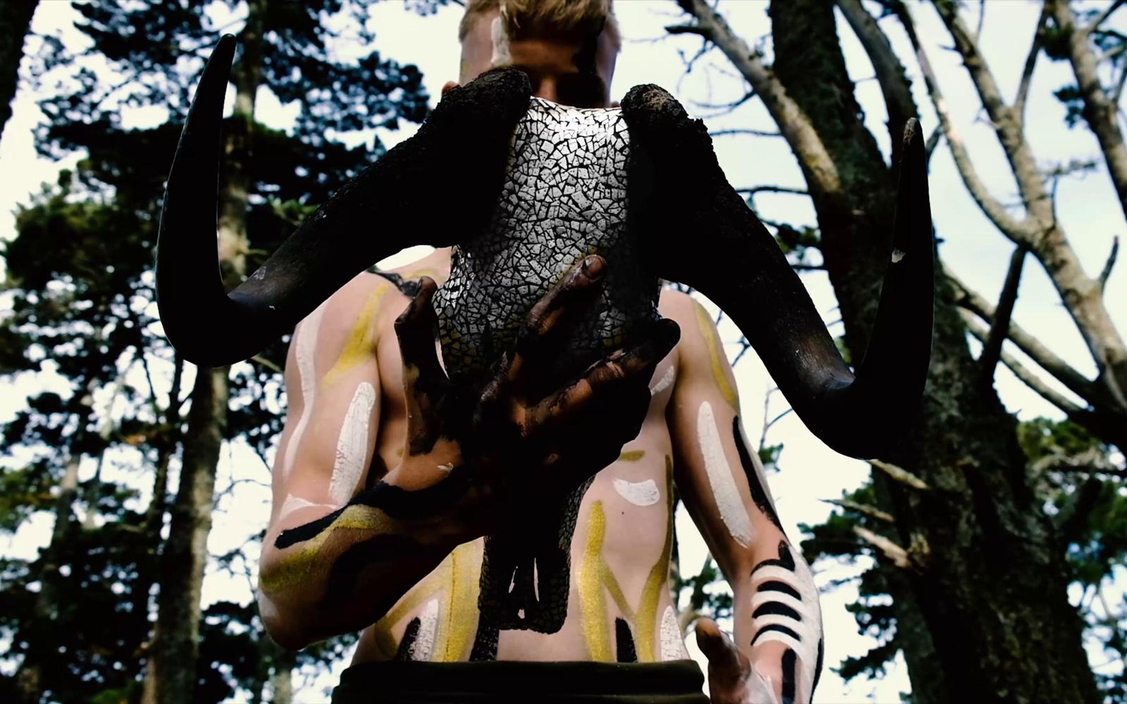 Performer carrying a horned skull over his shoulder in a high contrast black and white forest