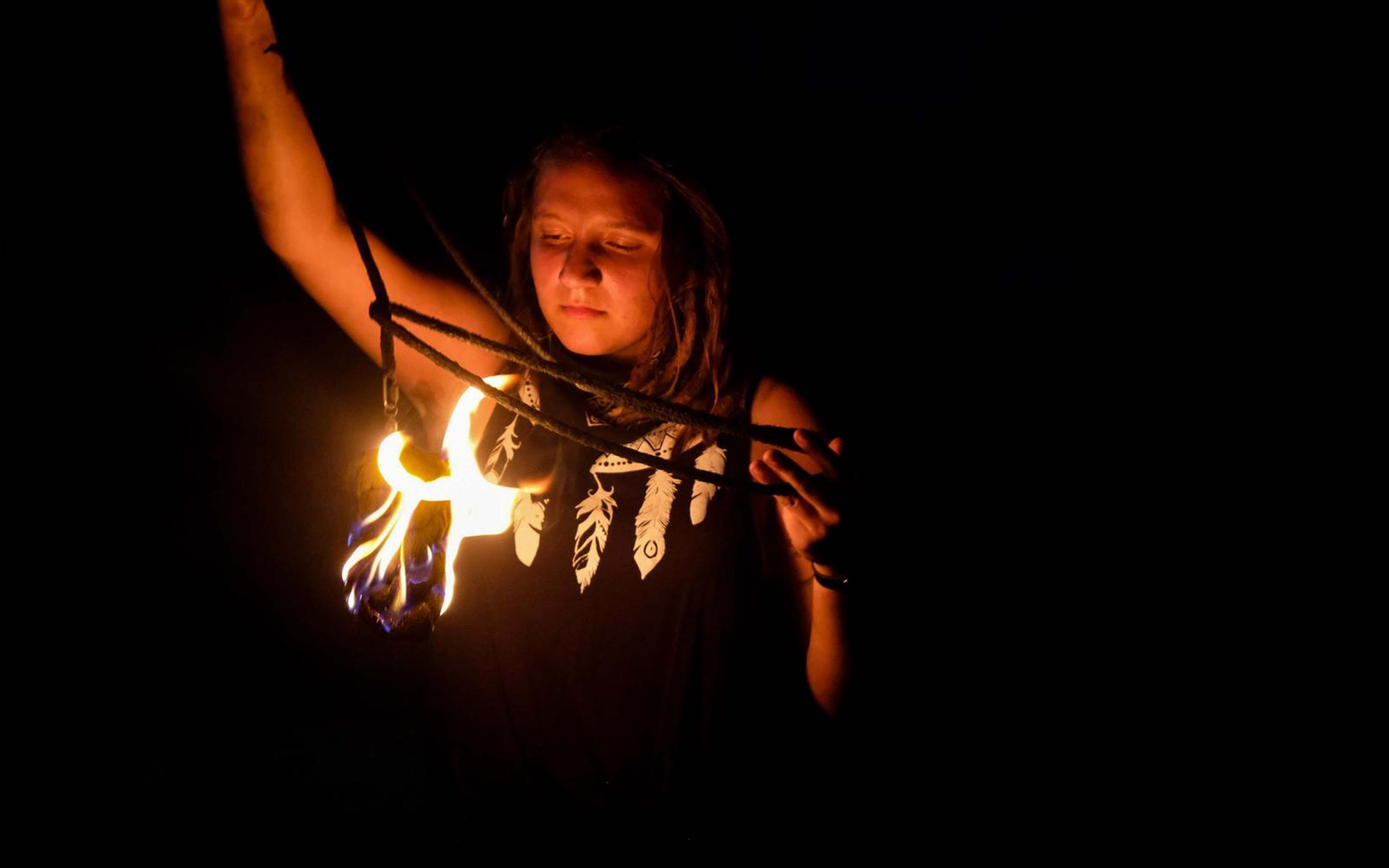 Performer looking down at a fire prop held at the chest, ropes in her hands and a feather-print top
