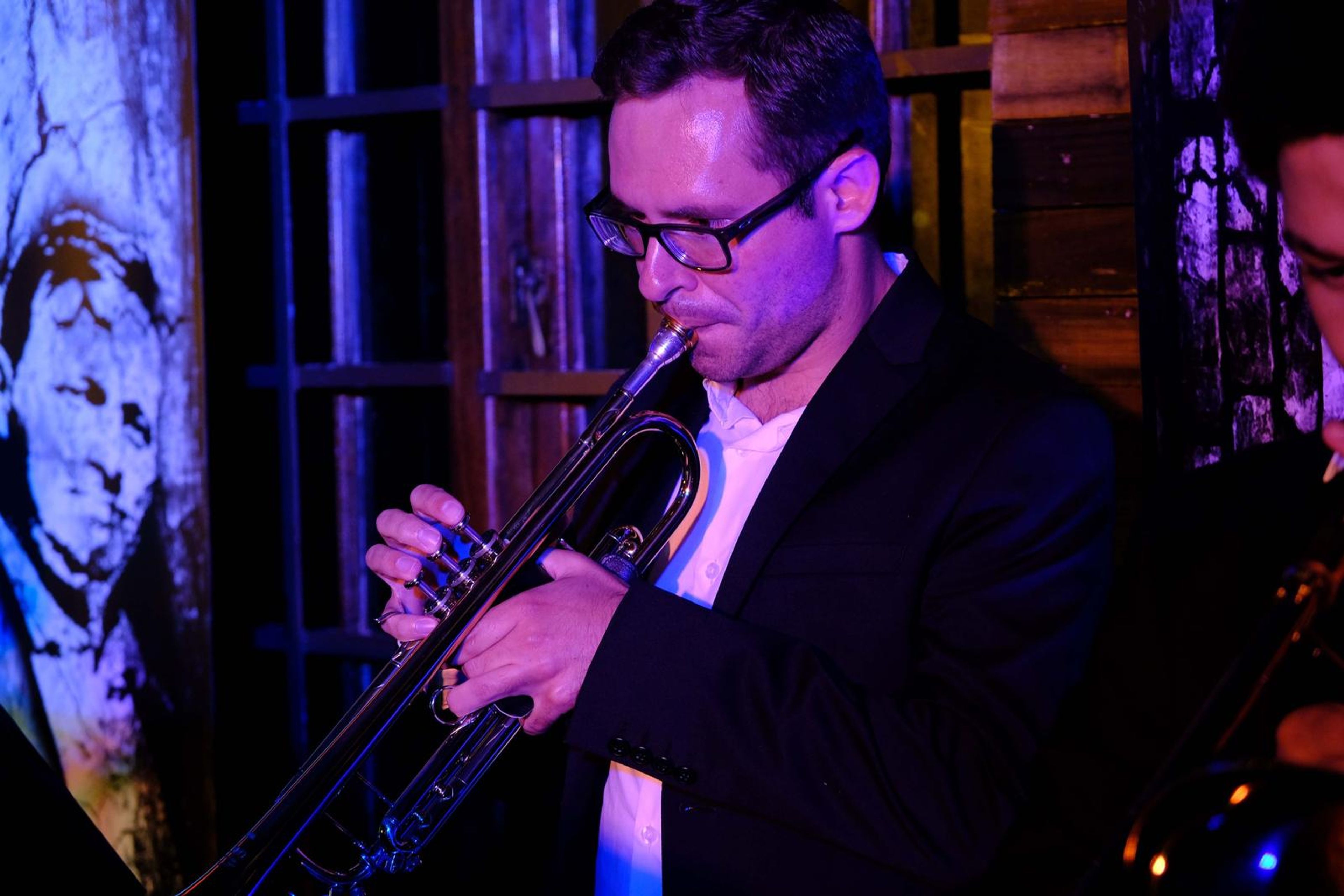 Trumpeter in glasses playing beside a mural wall
