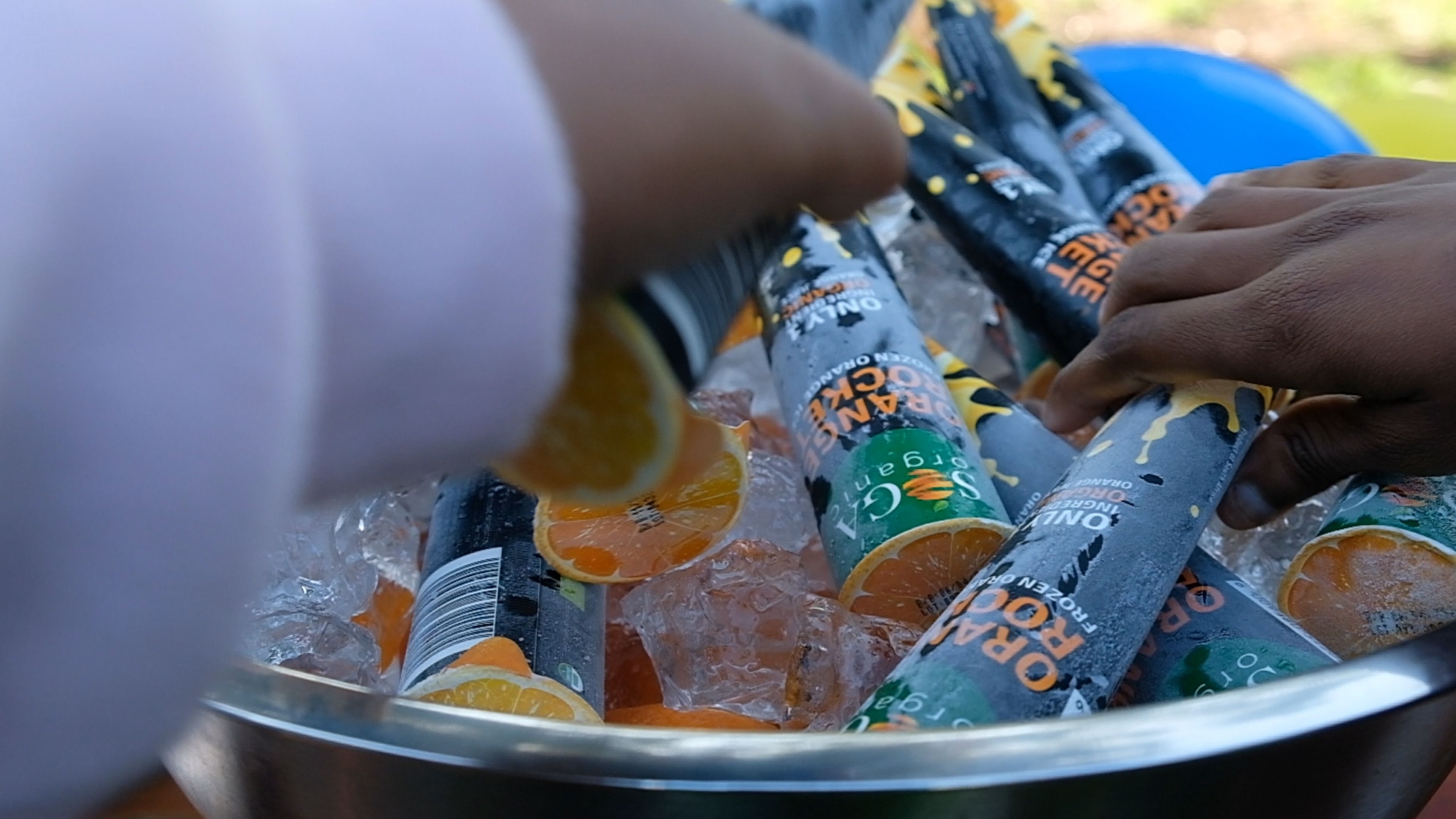 Hands reaching into a bowl of ice for Orange Rocket frozen ice tubes