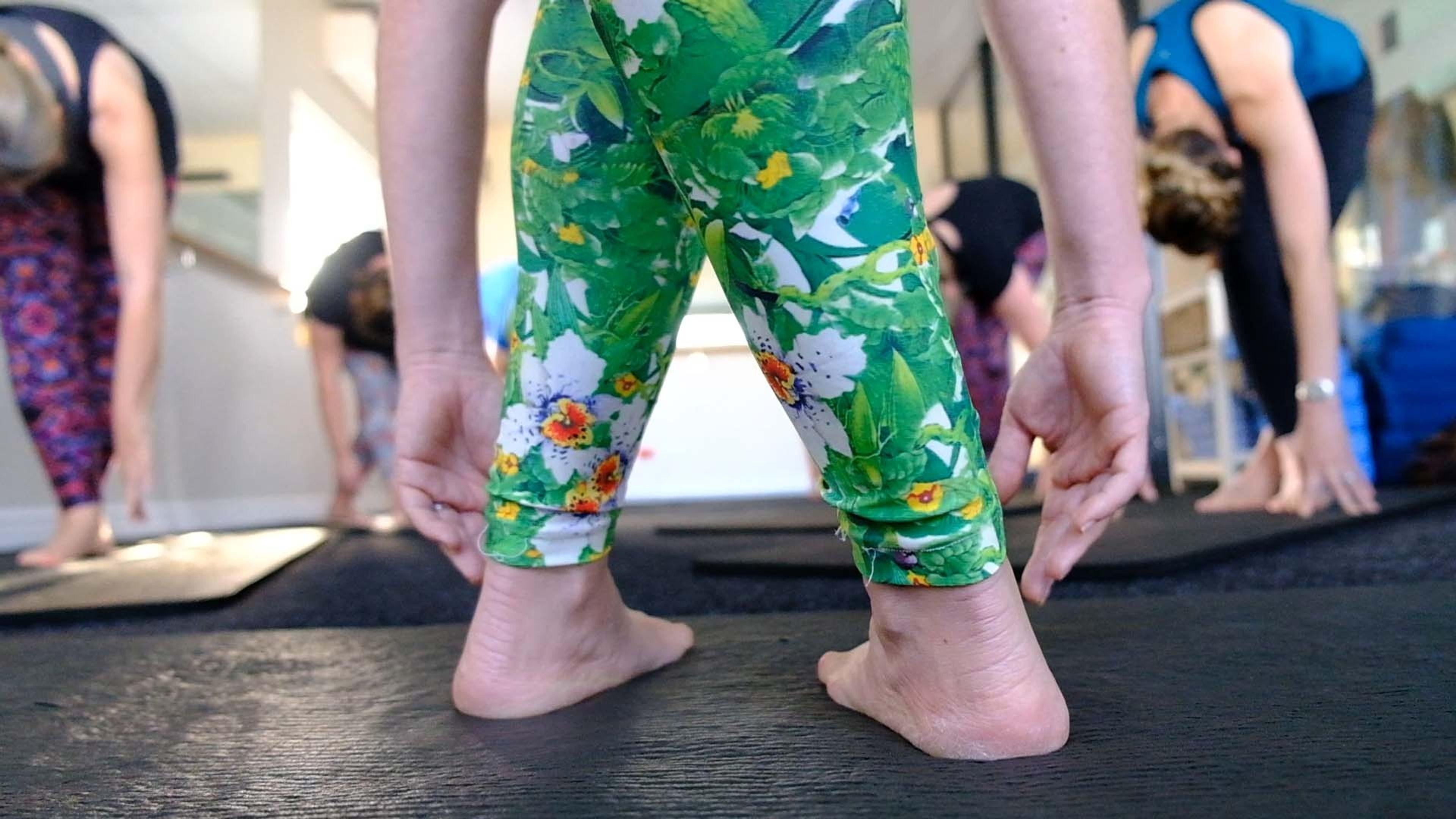 Legs in floral green leggings as a client folds forward on the studio floor