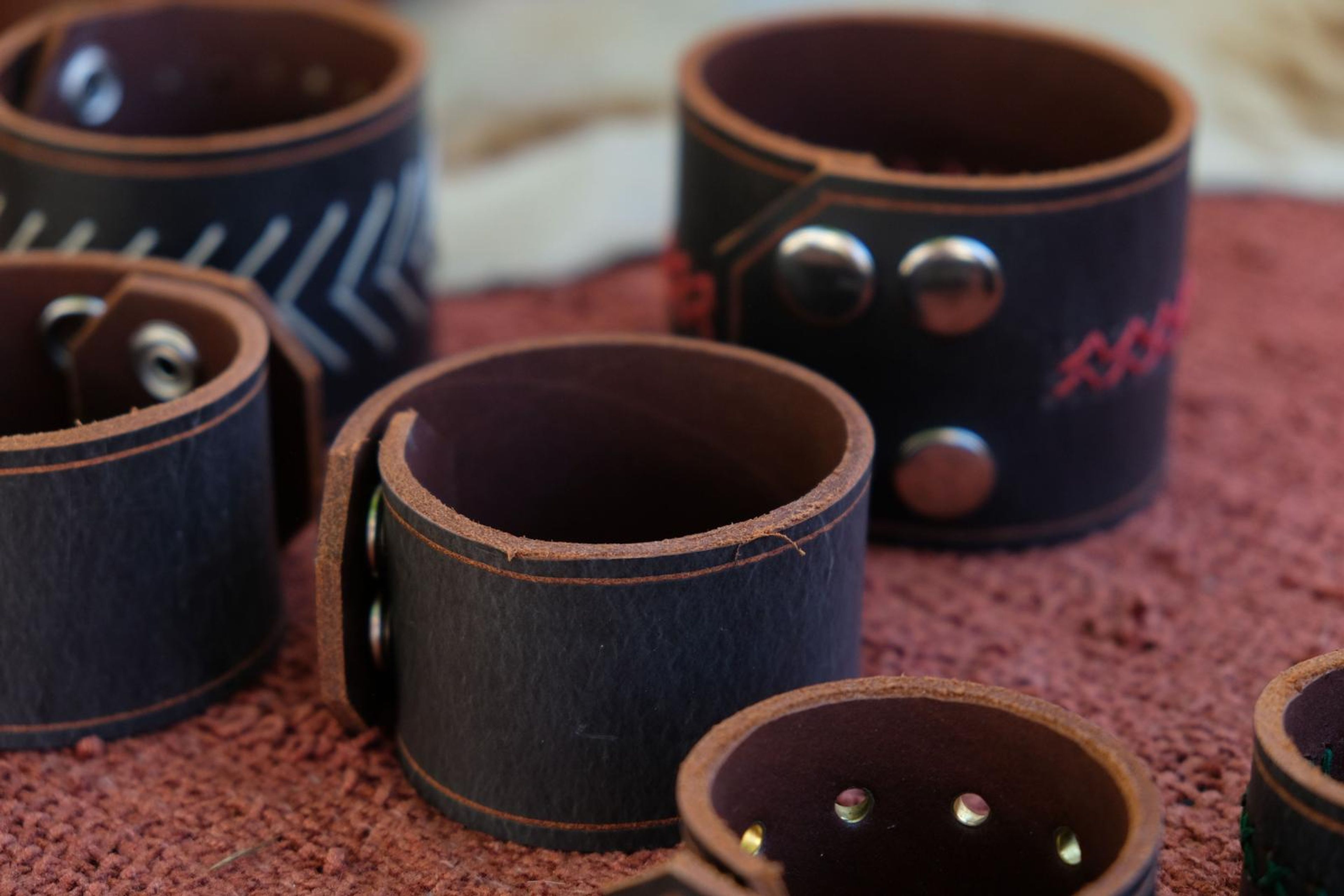 Dark leather cuffs with hand-stitched patterns on red cloth