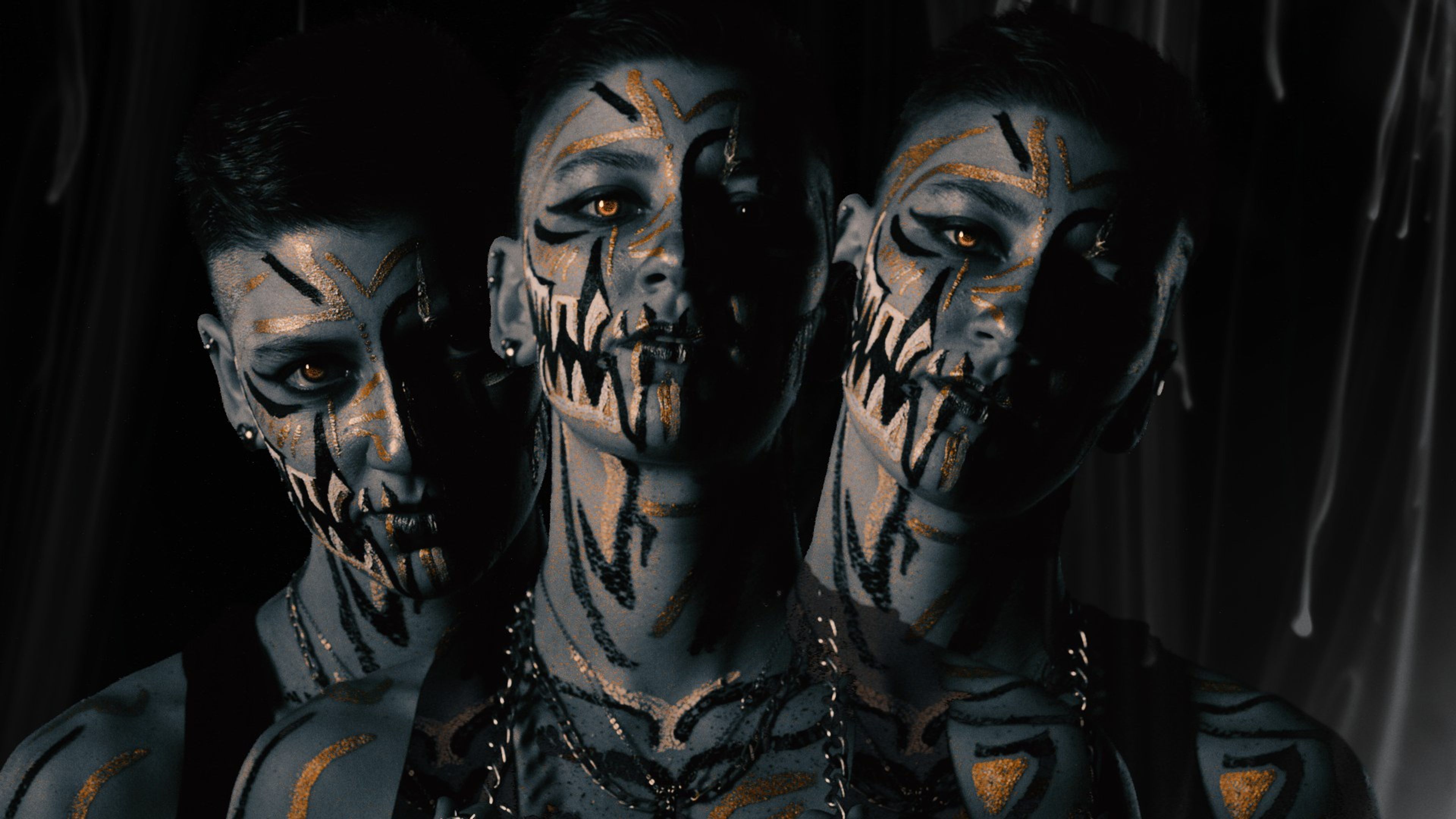 Three overlapping repeats of a face painted with black fang markings and a glowing amber eye