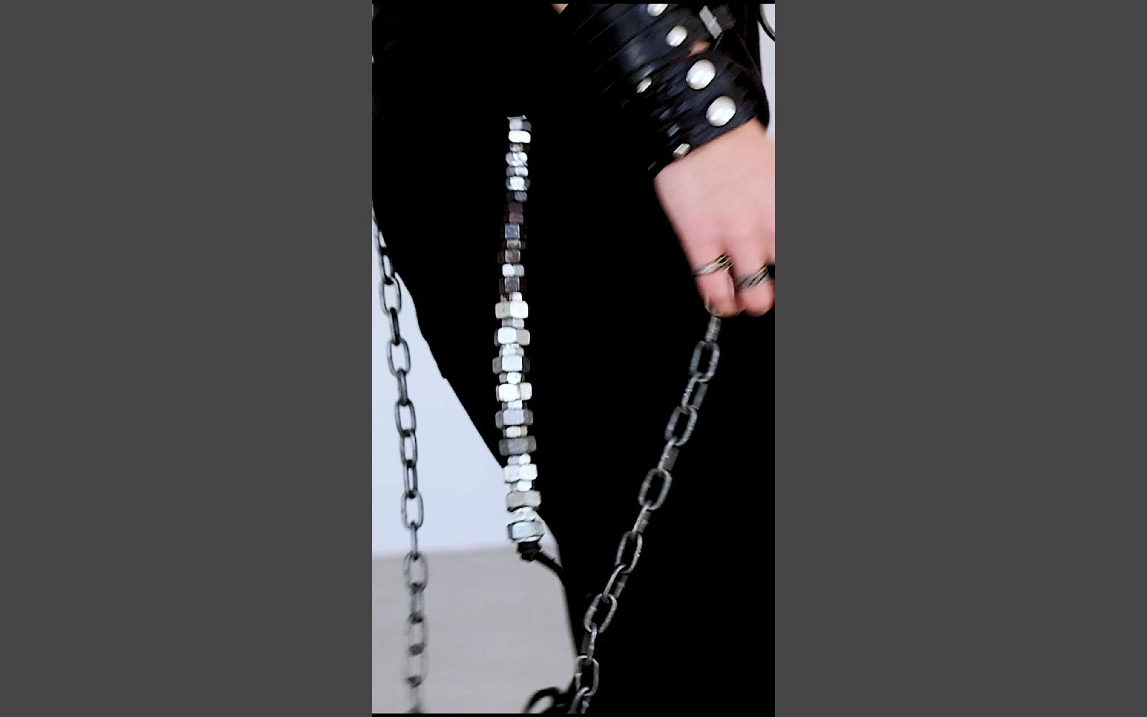 Close view of a studded wrist cuff, rings and a hanging chain with hex nuts