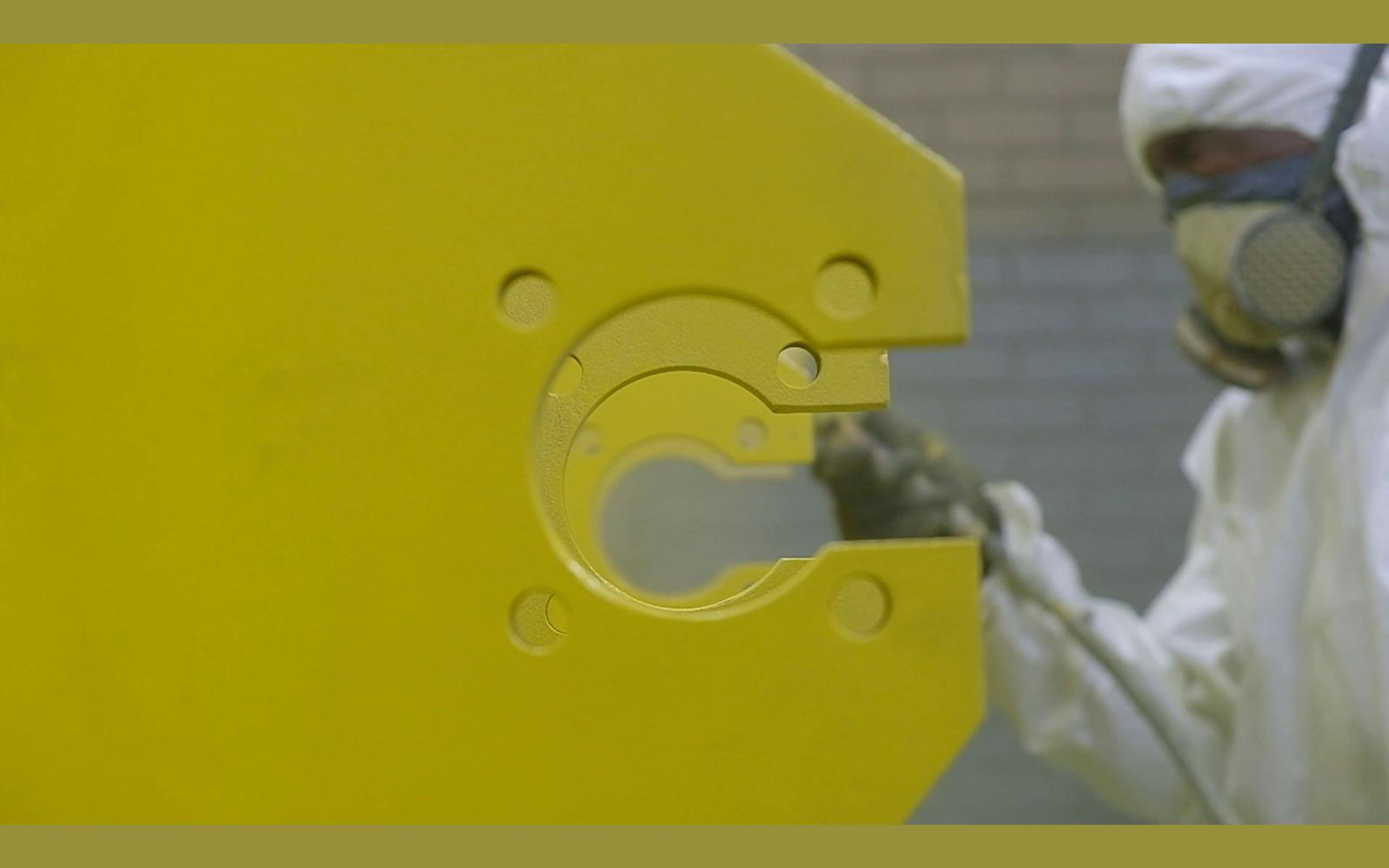 Spray gun painting a yellow steel plate with round cut-outs