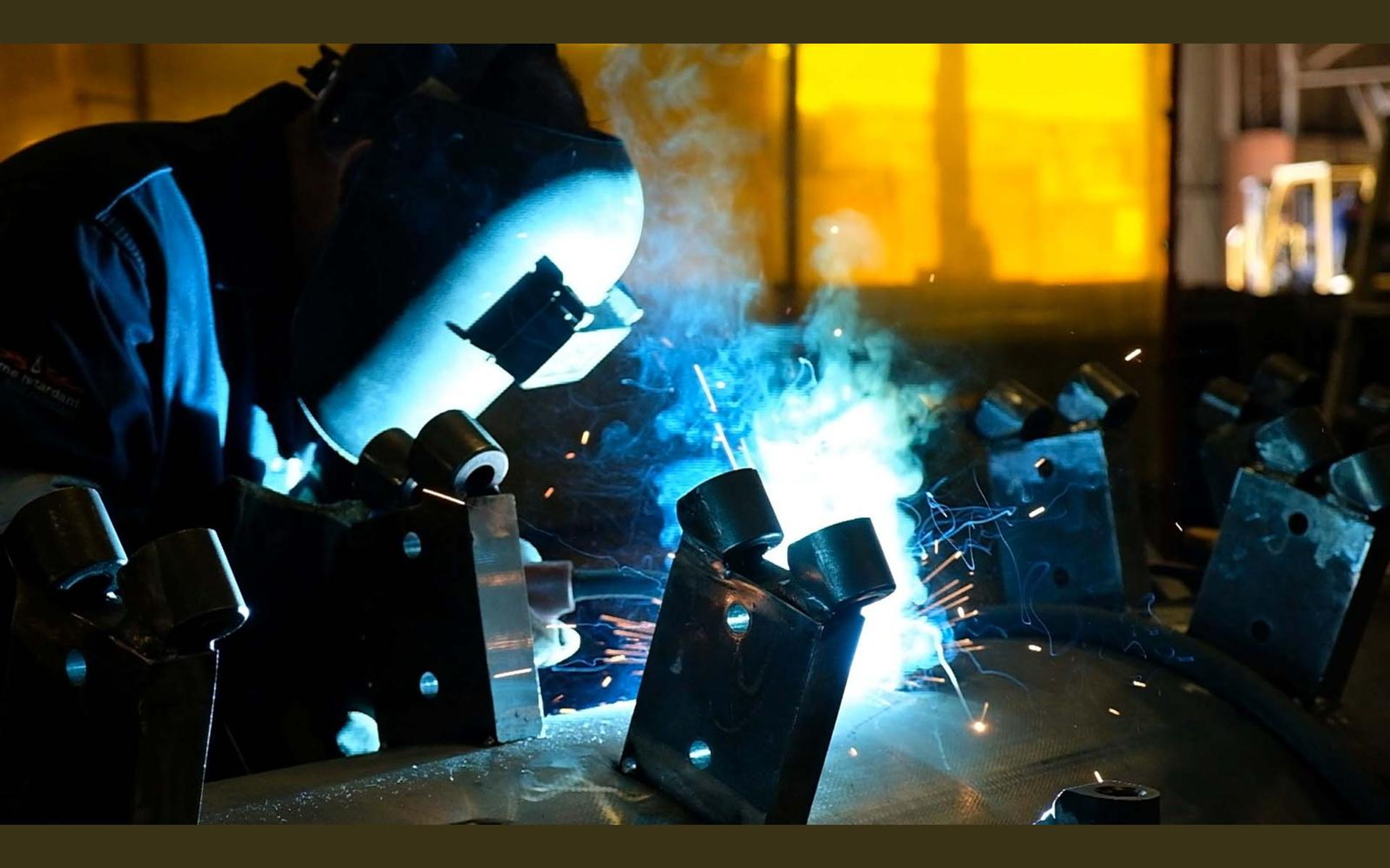 Welder welding steel brackets on a large drum with a bright arc