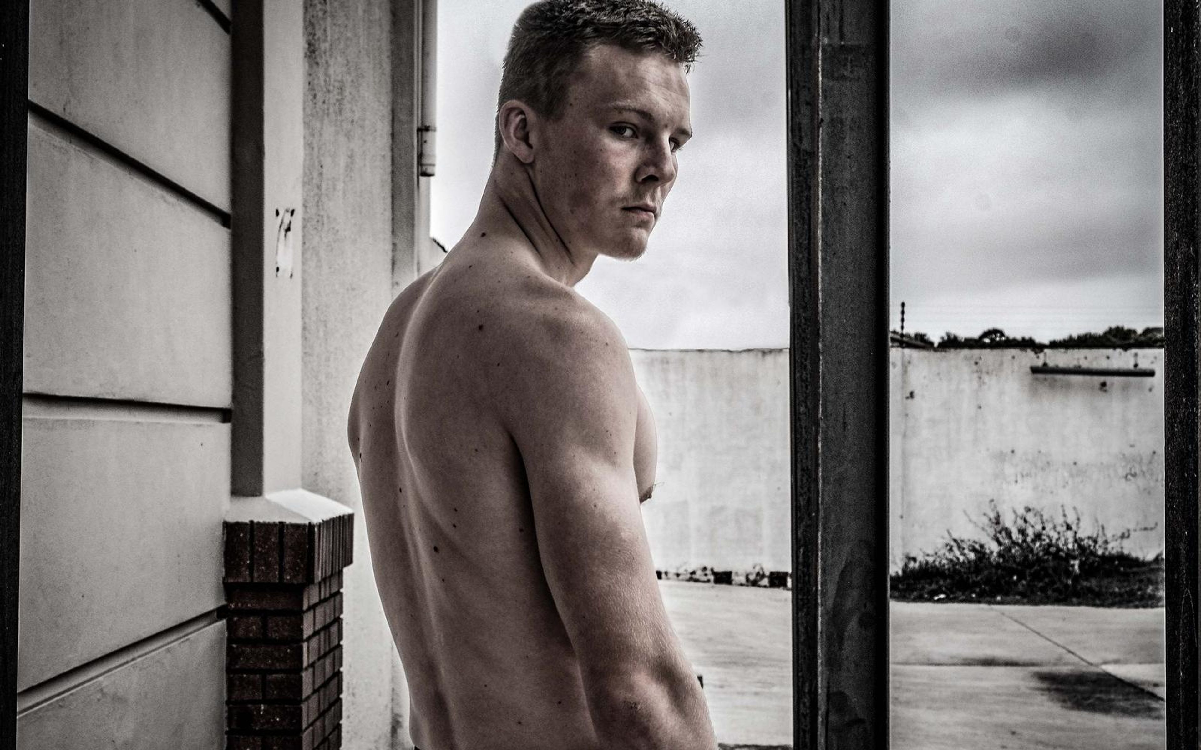 Man looking back over his shoulder in a muted tone, doorway and concrete wall behind him