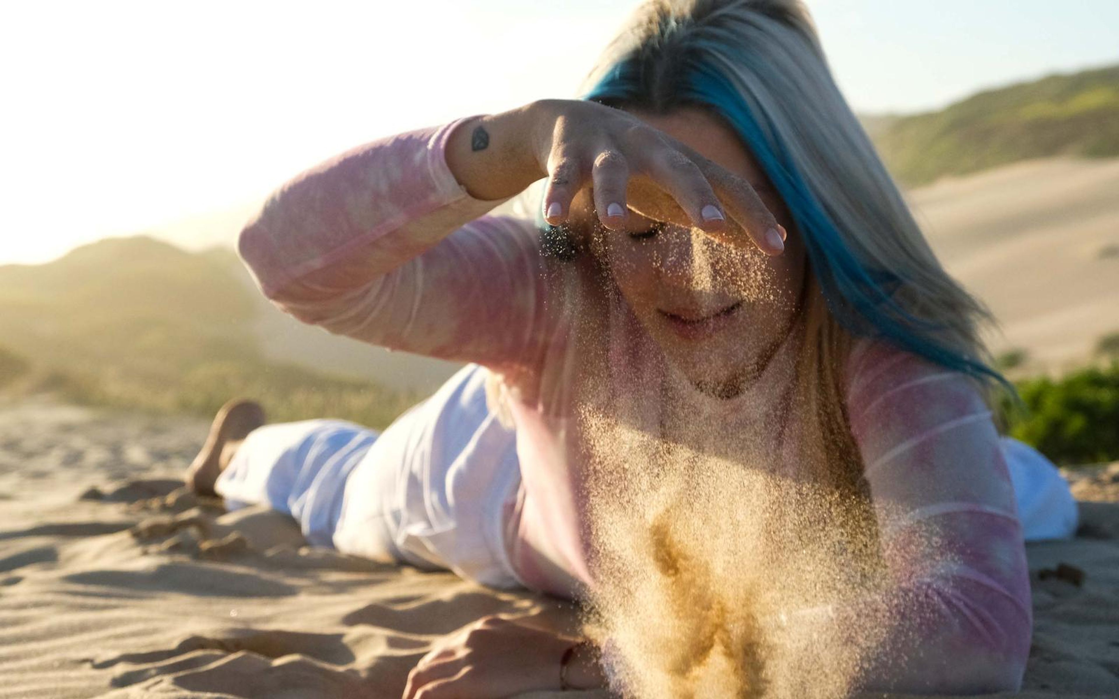 Woman lying on the sand with a hand over her eyes as sand falls from her fingers