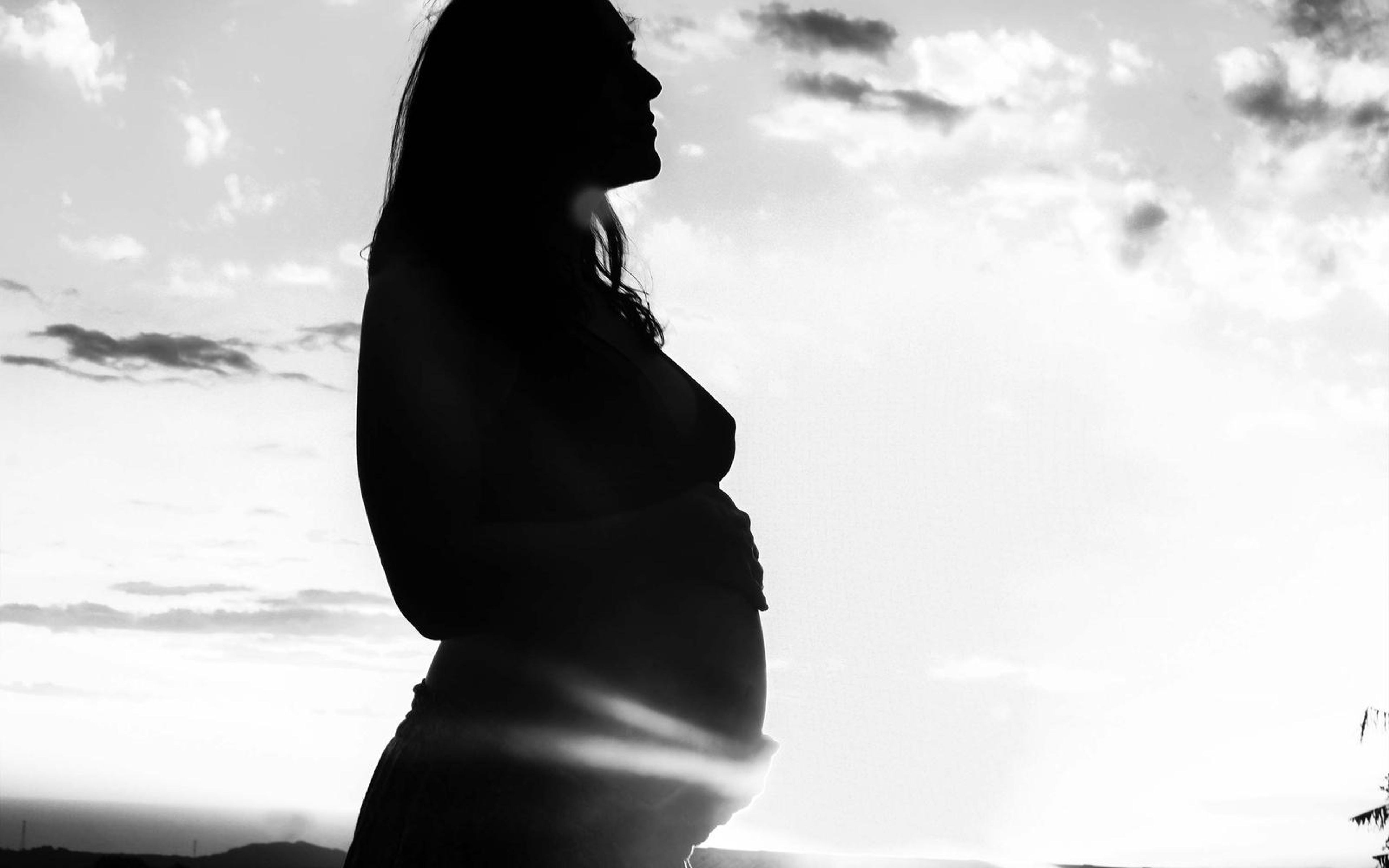 High-key black and white silhouette of a pregnant woman, profile with lifted chin, flare near her belly
