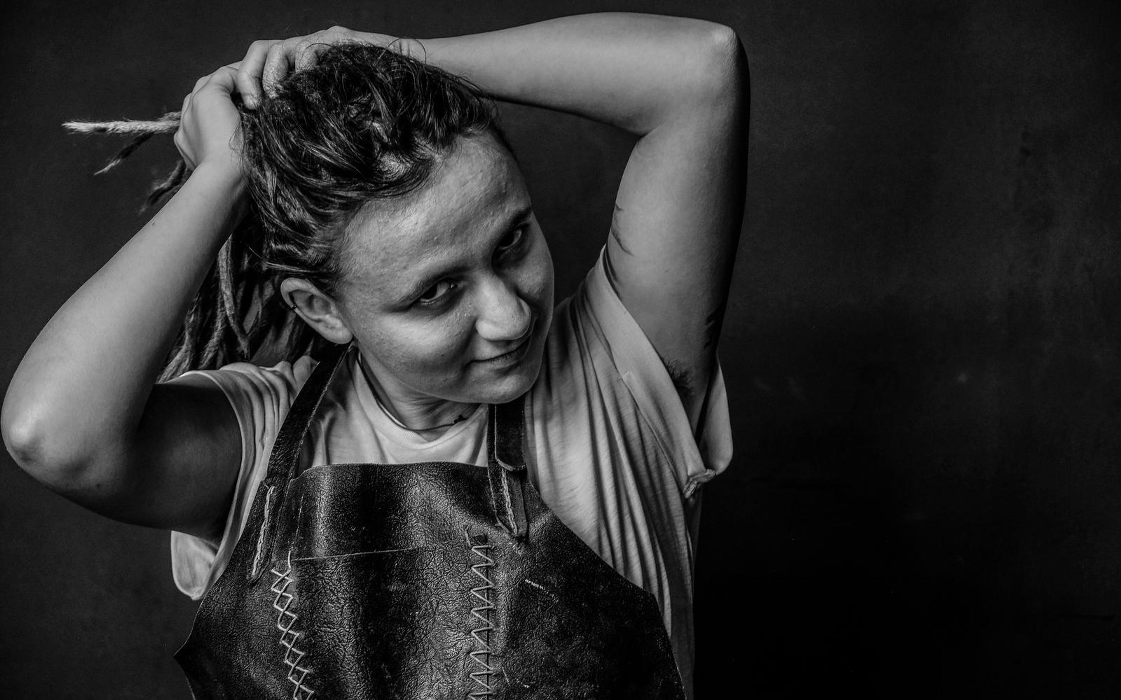Black and white portrait of a woman with both hands in her dreadlocks, looking sideways over her shoulder