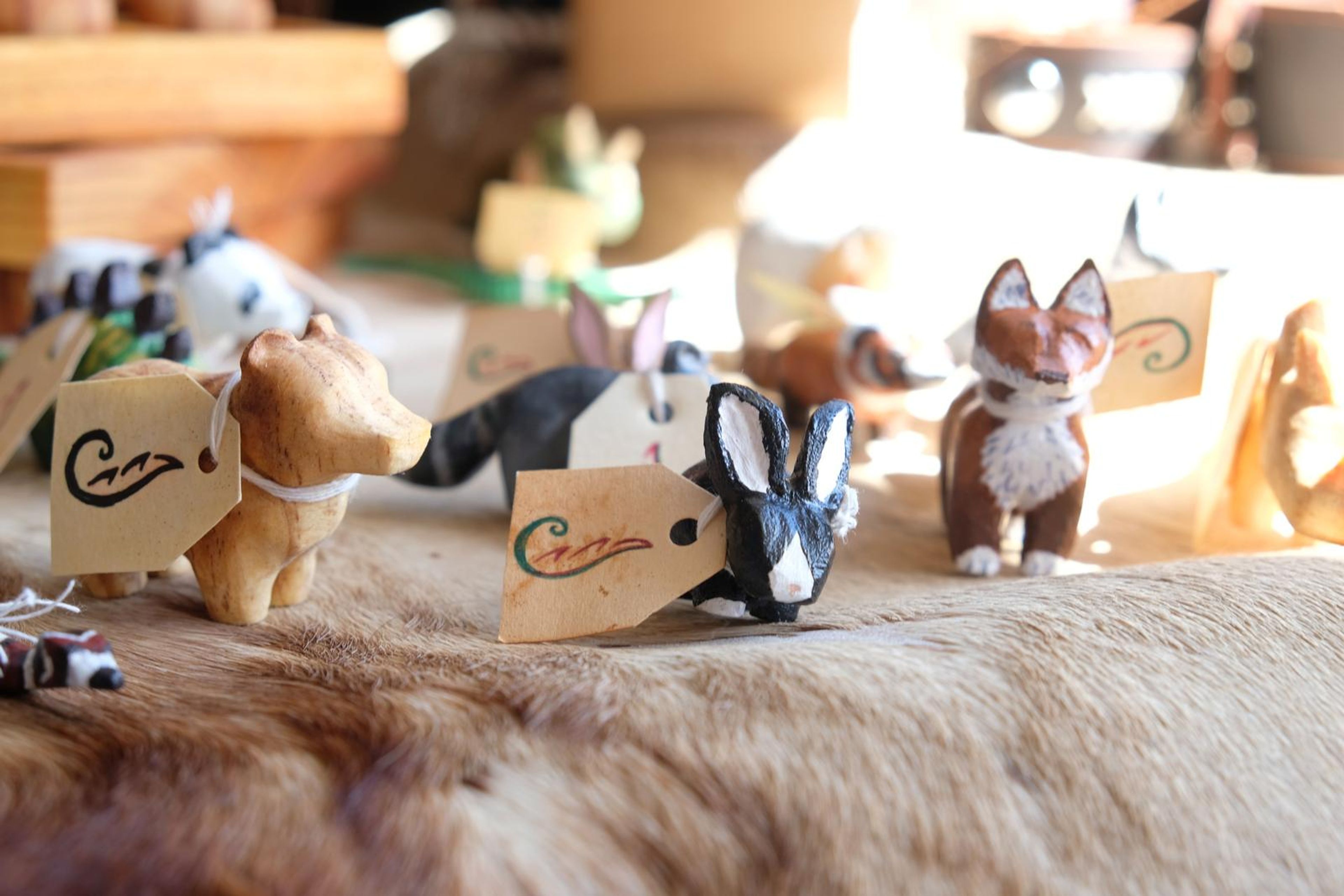 Hand-painted carved wooden animal figures with handwritten tags on a fur