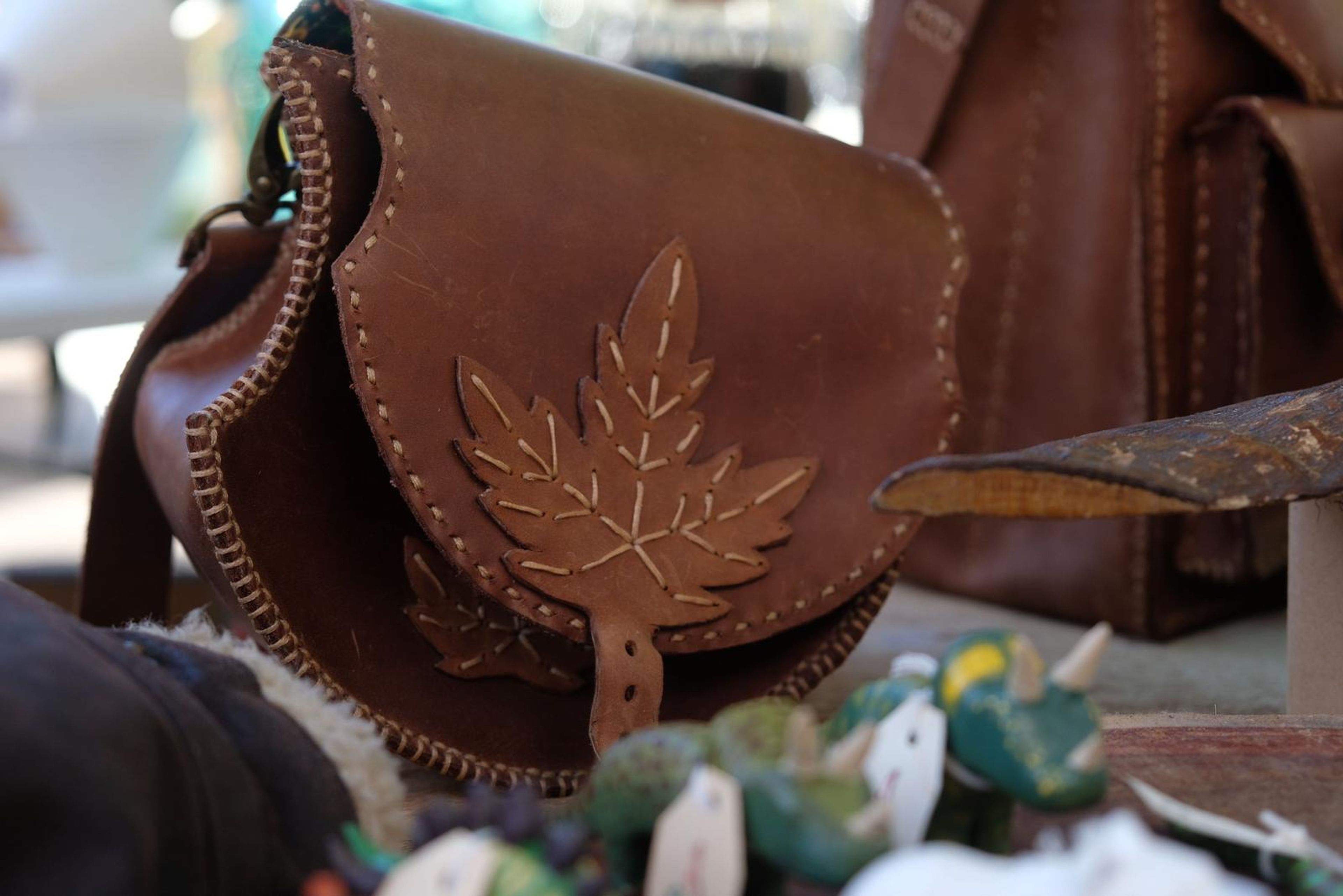 Brown leather pouch with a pressed maple leaf design and stitched edge
