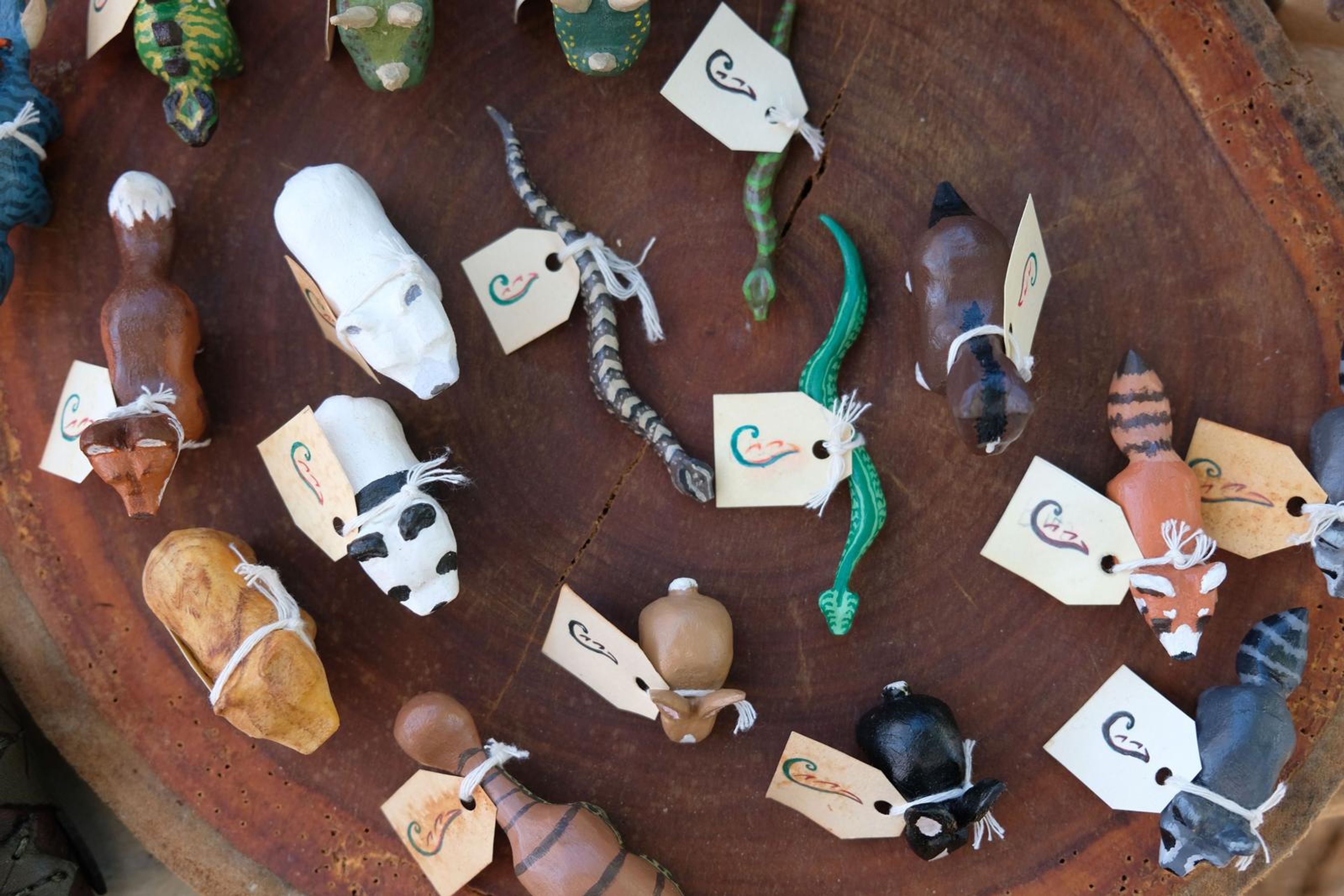 Hand-carved wooden animal figures with handwritten tags on a log slice