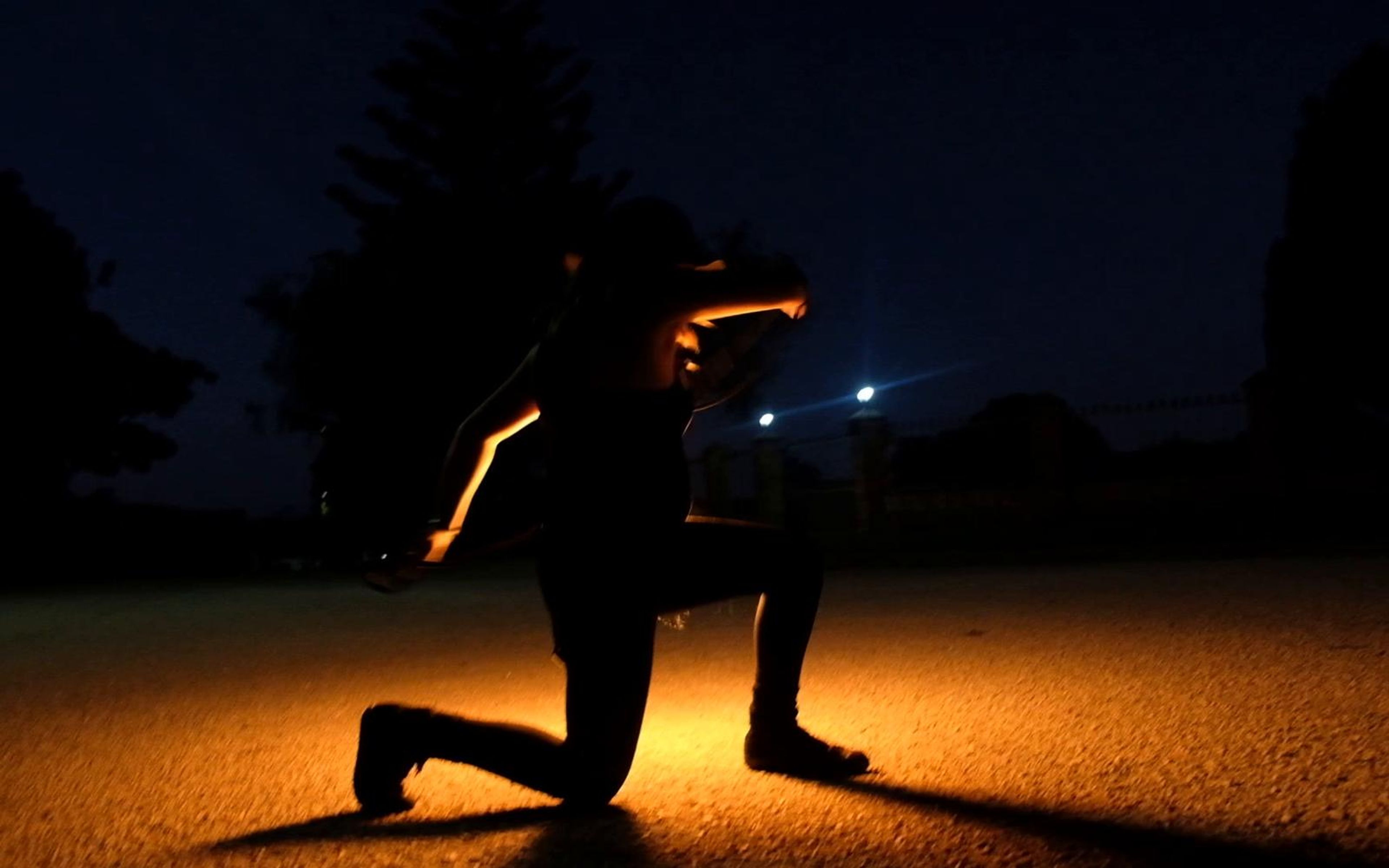 Performer kneeling on gravel with a fire prop trailing light at night