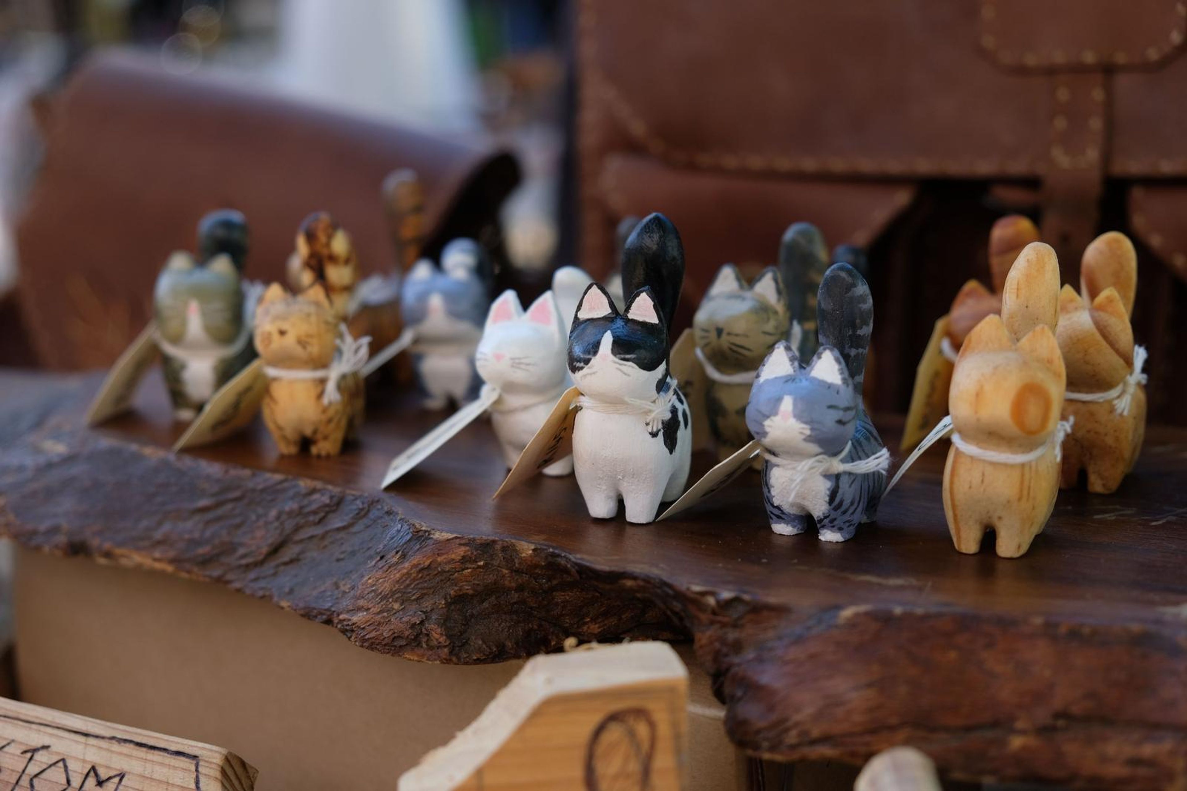 Hand-carved wooden cats on a bark shelf beside a leather satchel