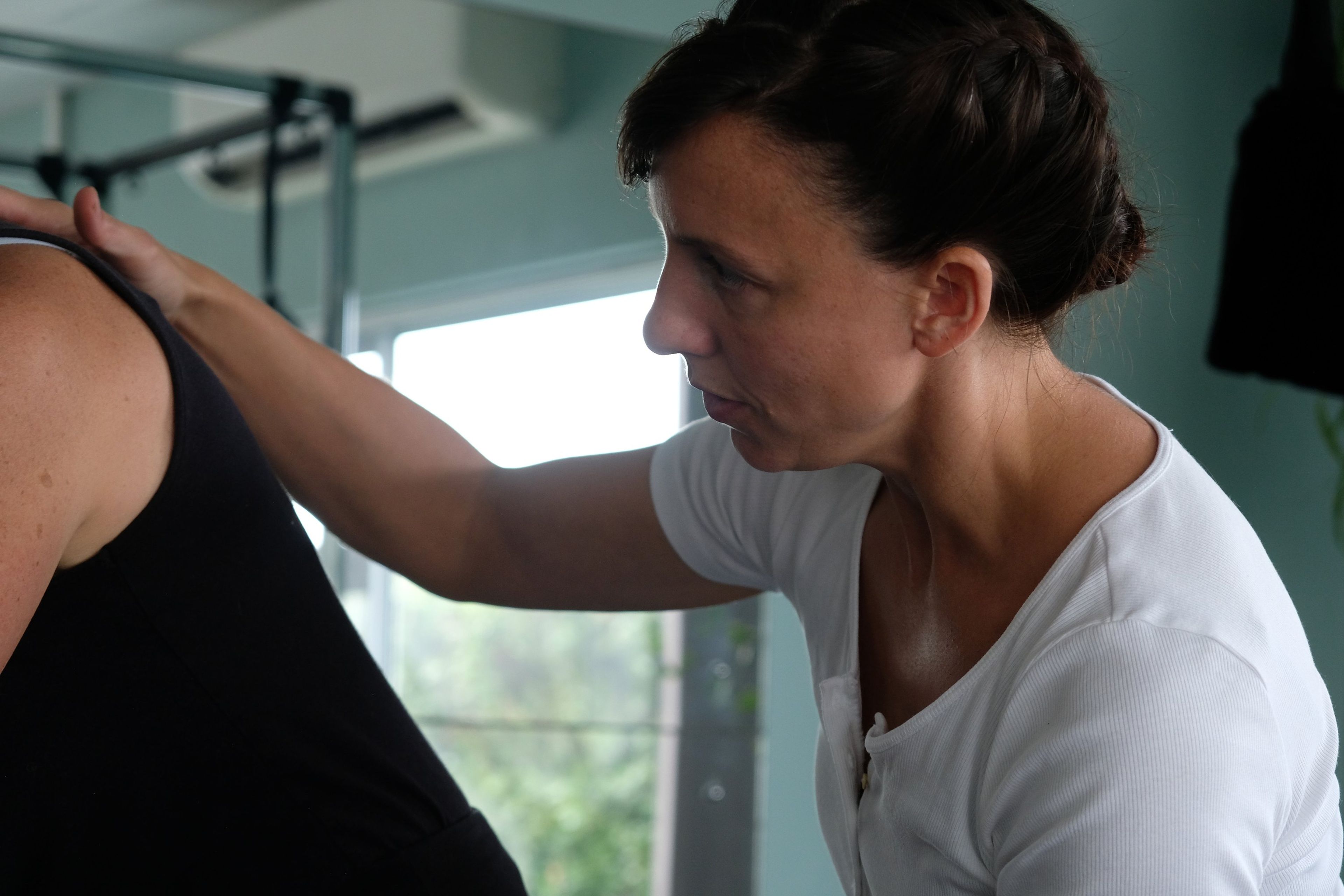 Instructor in a white top placing a hand on a client's shoulder to correct her position