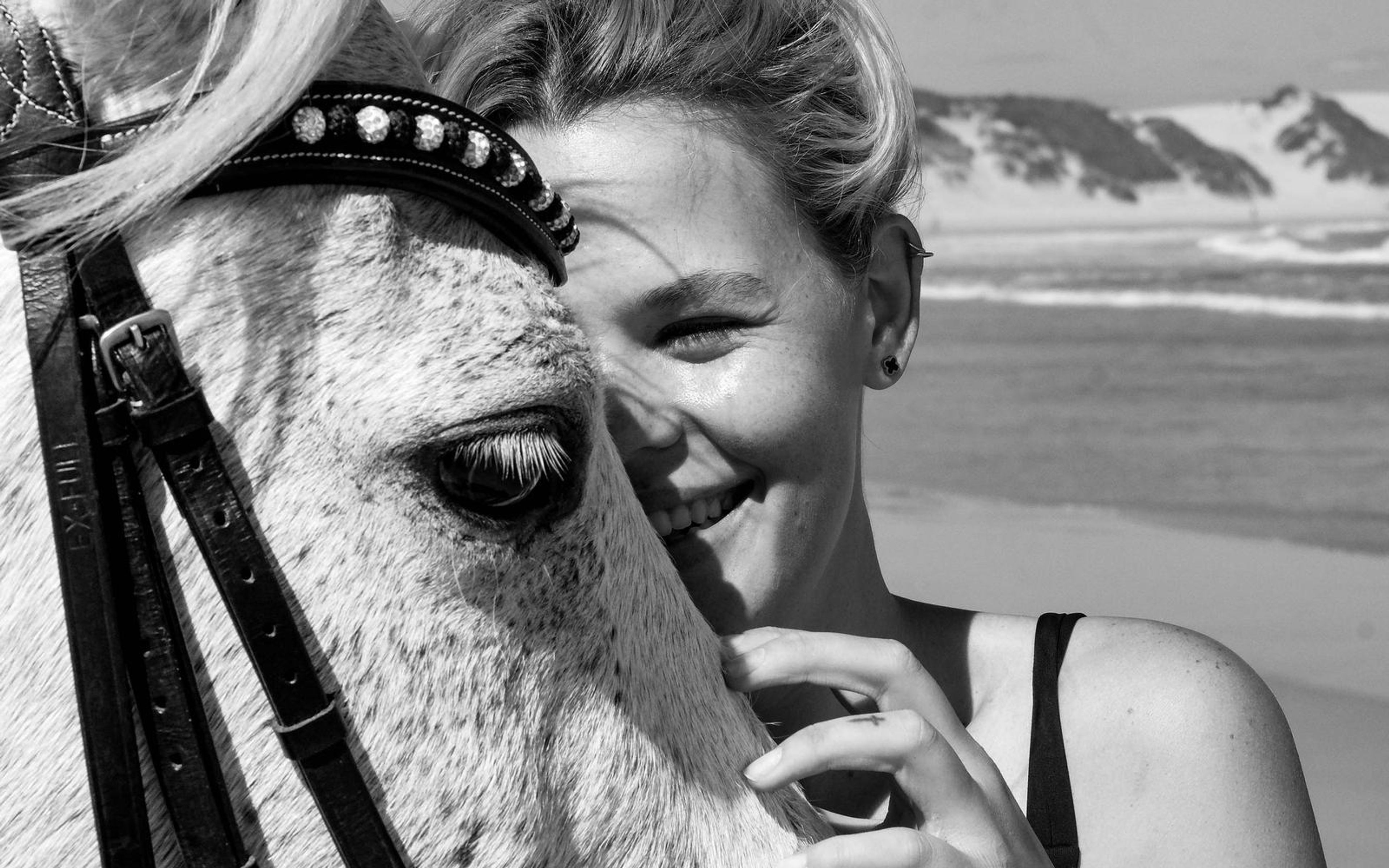 Black and white version of a woman smiling beside a white horse, wave line behind