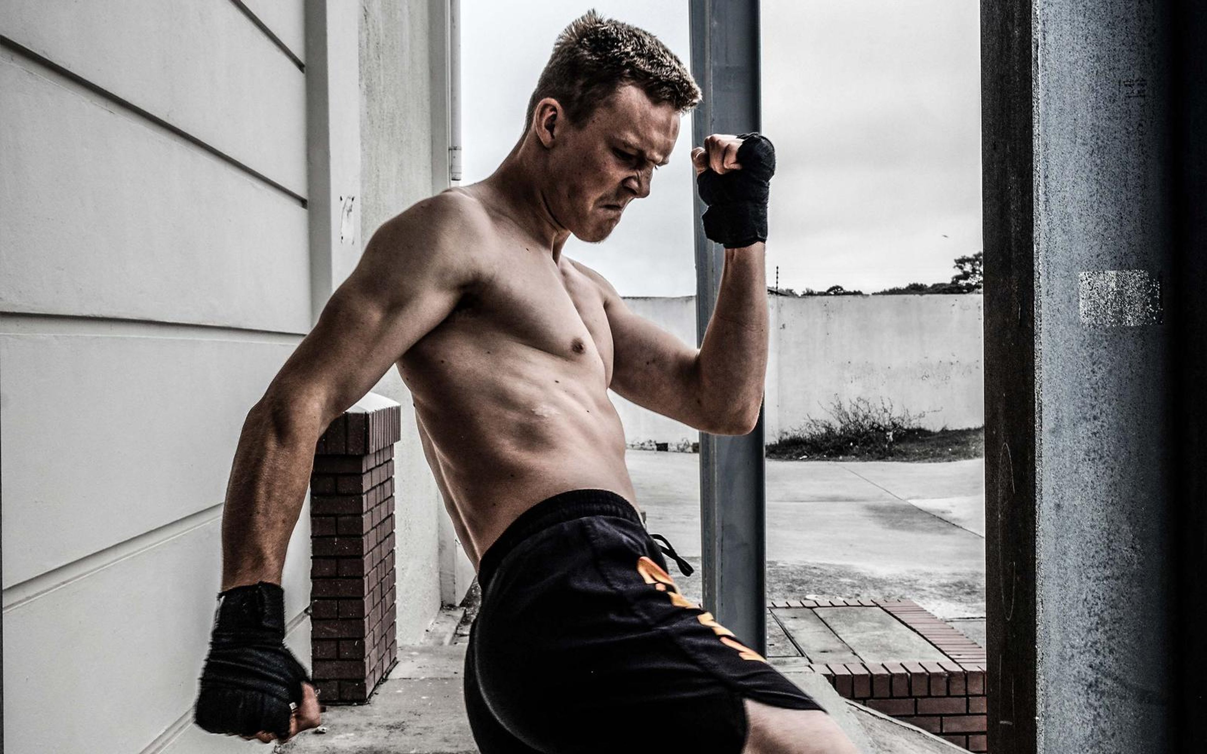 Fighter leaning on a steel pole with a wrapped fist raised, bare torso and black shorts