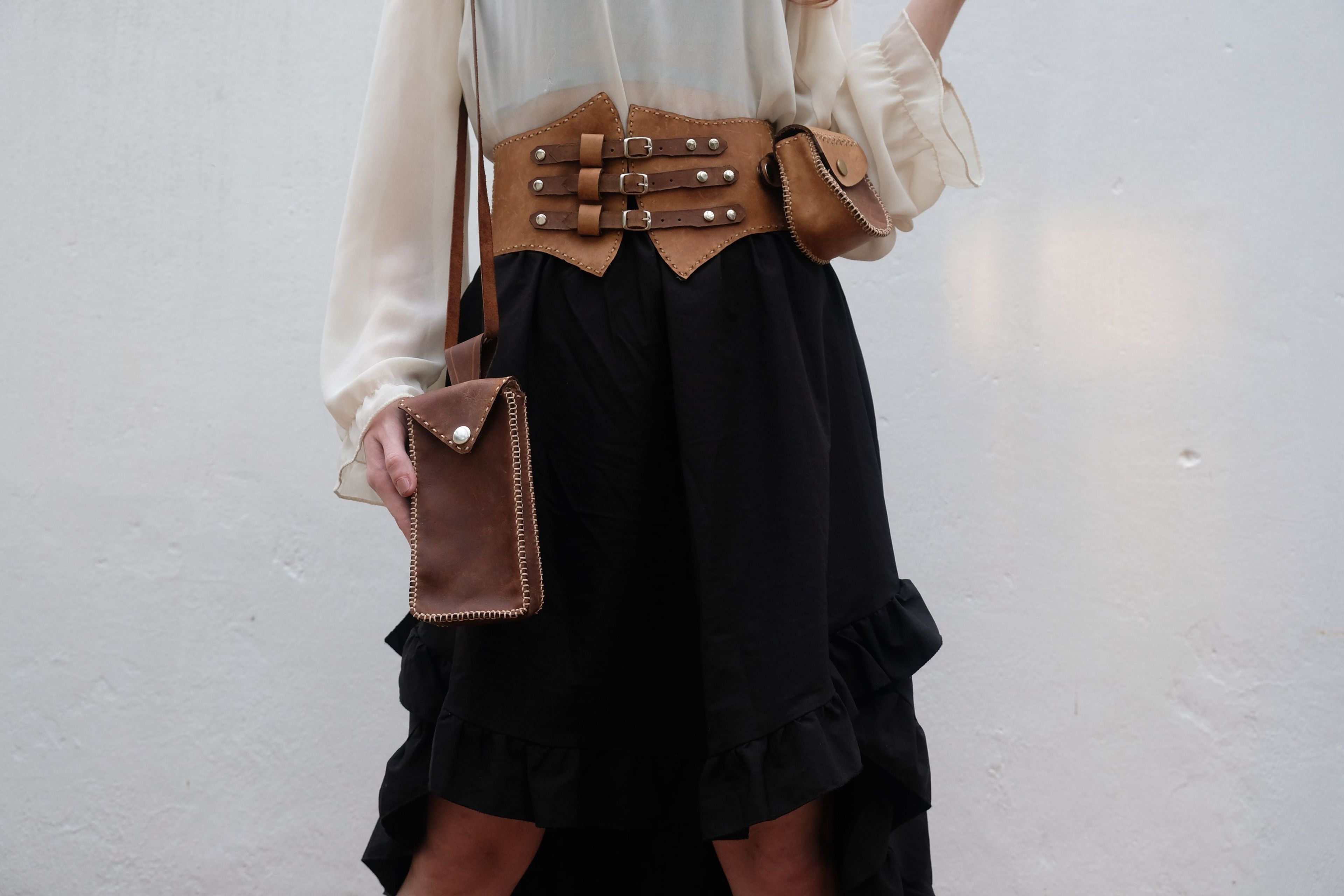 Woman in a leather corset belt with a brown phone bag hanging at her side