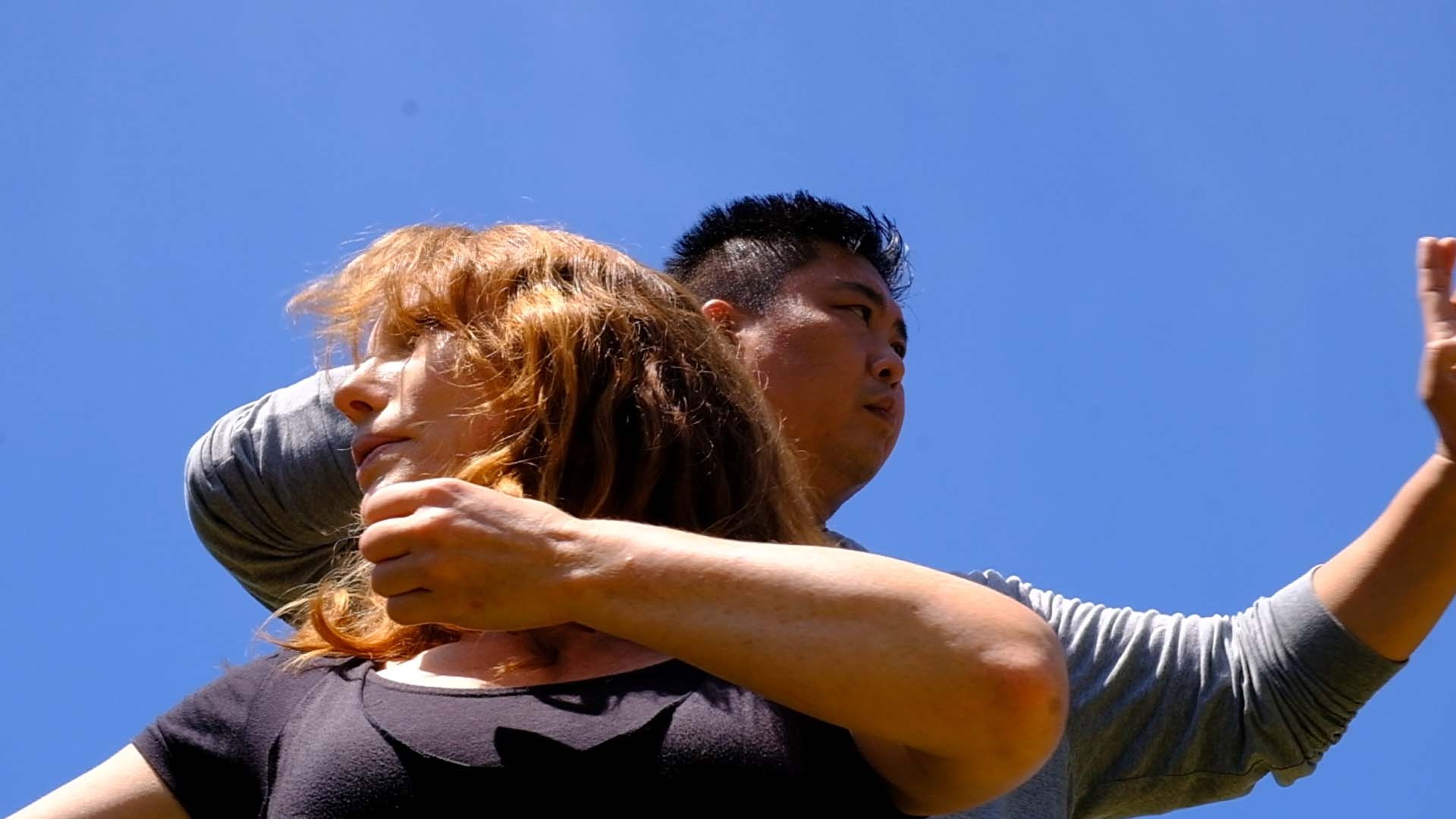 Close view of a partnered outdoor movement session, the woman's arm crossing her chest