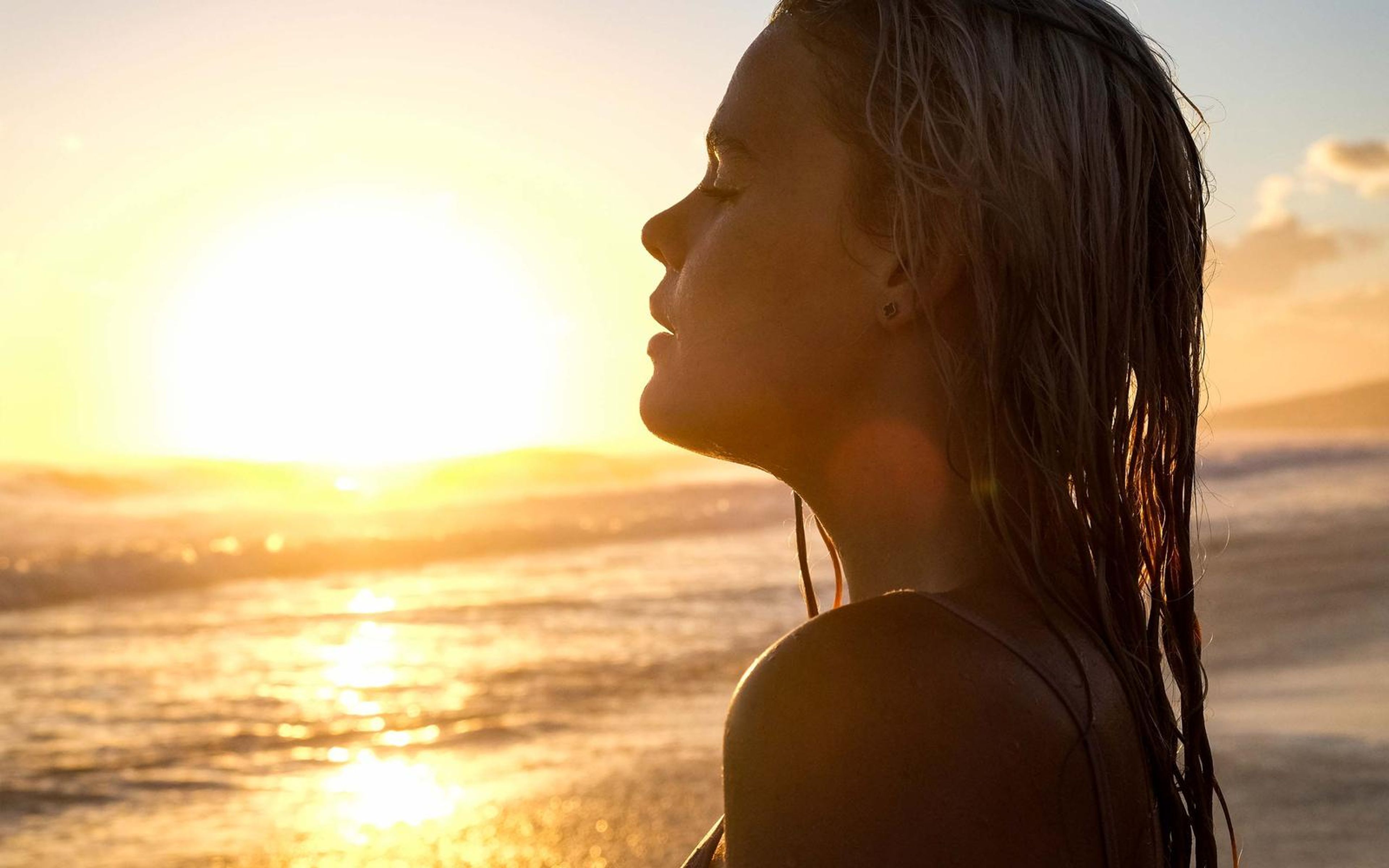 Profile of a woman with wet hair against a golden horizon, face turned to the sun