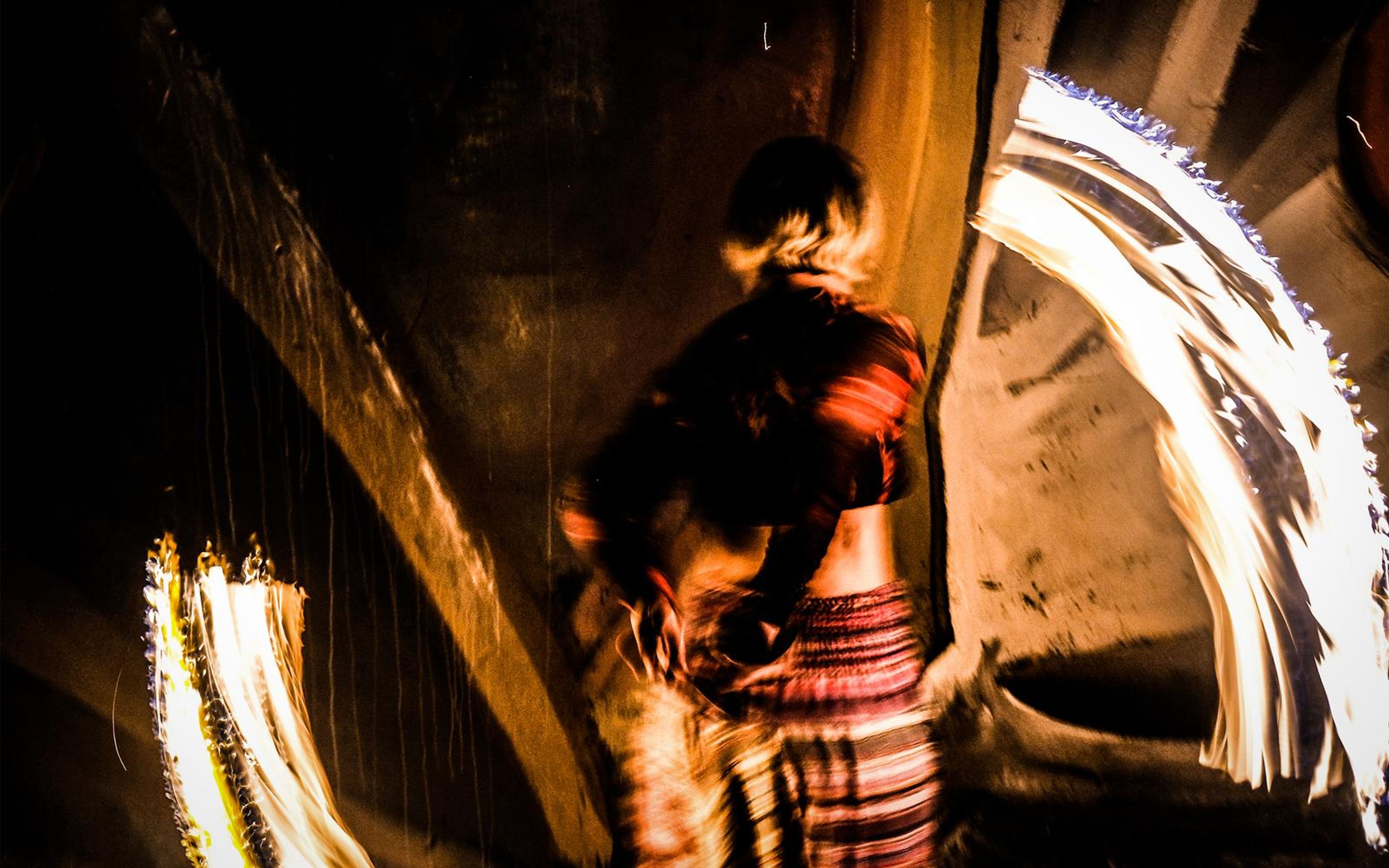 Performer turning away as a bright white arc of fire light sweeps across the right of the frame