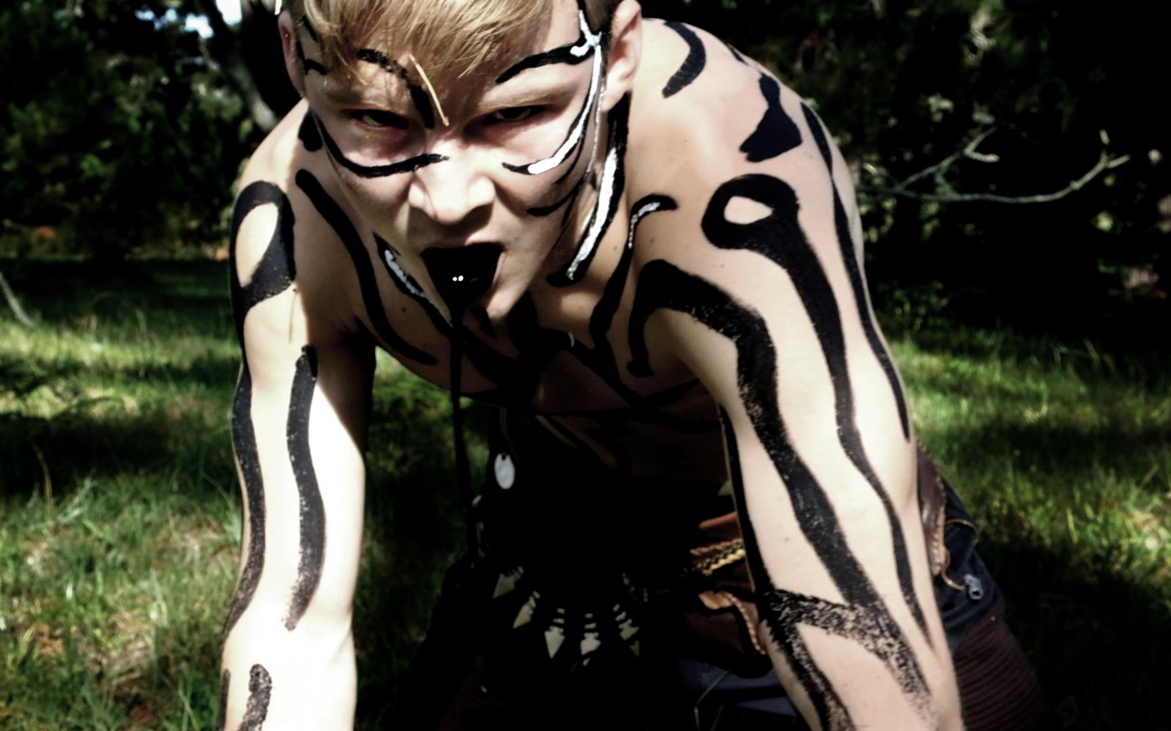 Painted performer crouching on grass with black tiger-stripe body paint and an intense stare