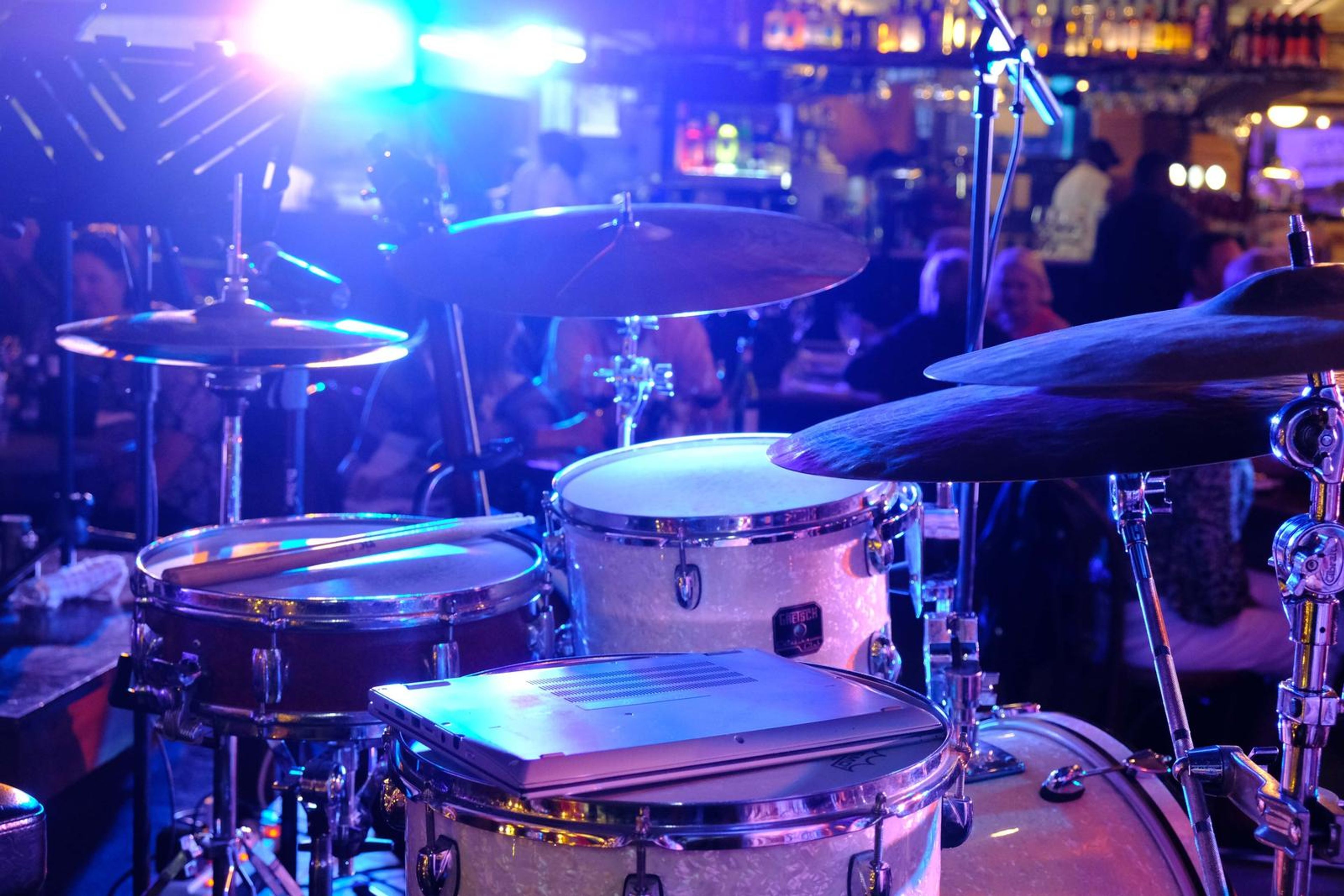 Drum kit under blue light with the restaurant crowd behind